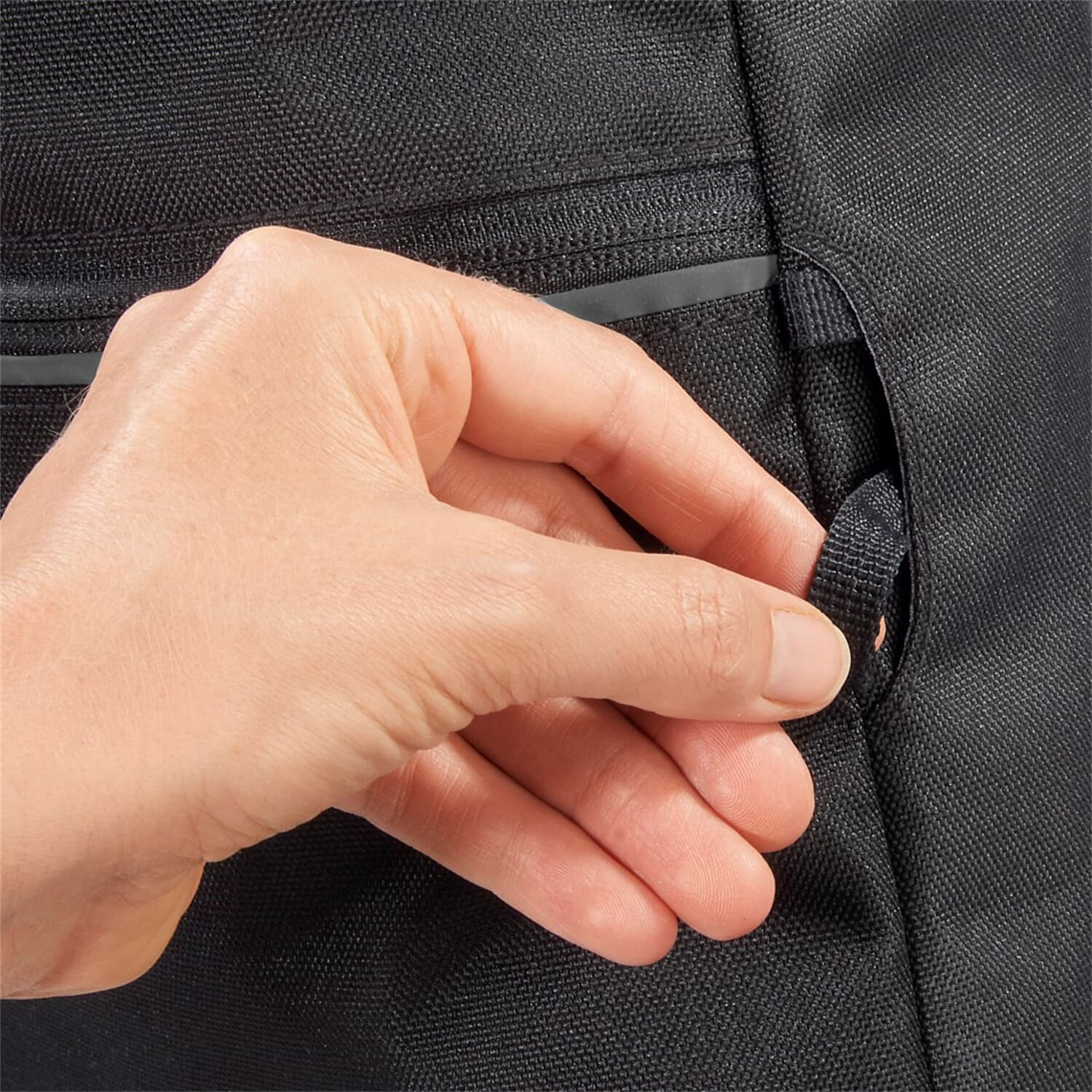 Hand öffnet eine schwarze Taschentasche, mit sichtbarem Reißverschluss.