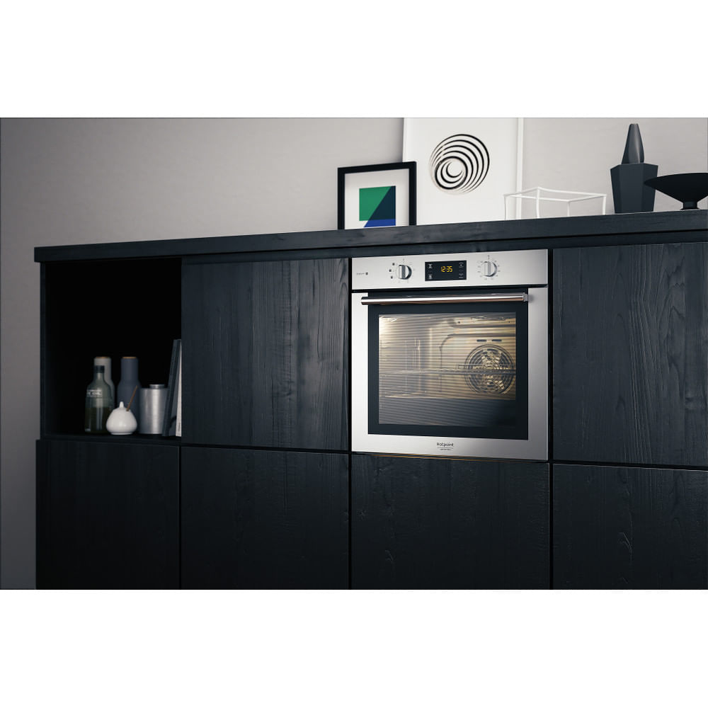 Forno integrato in un mobile nero. Opere d'arte e bottiglie visibili sopra il forno.