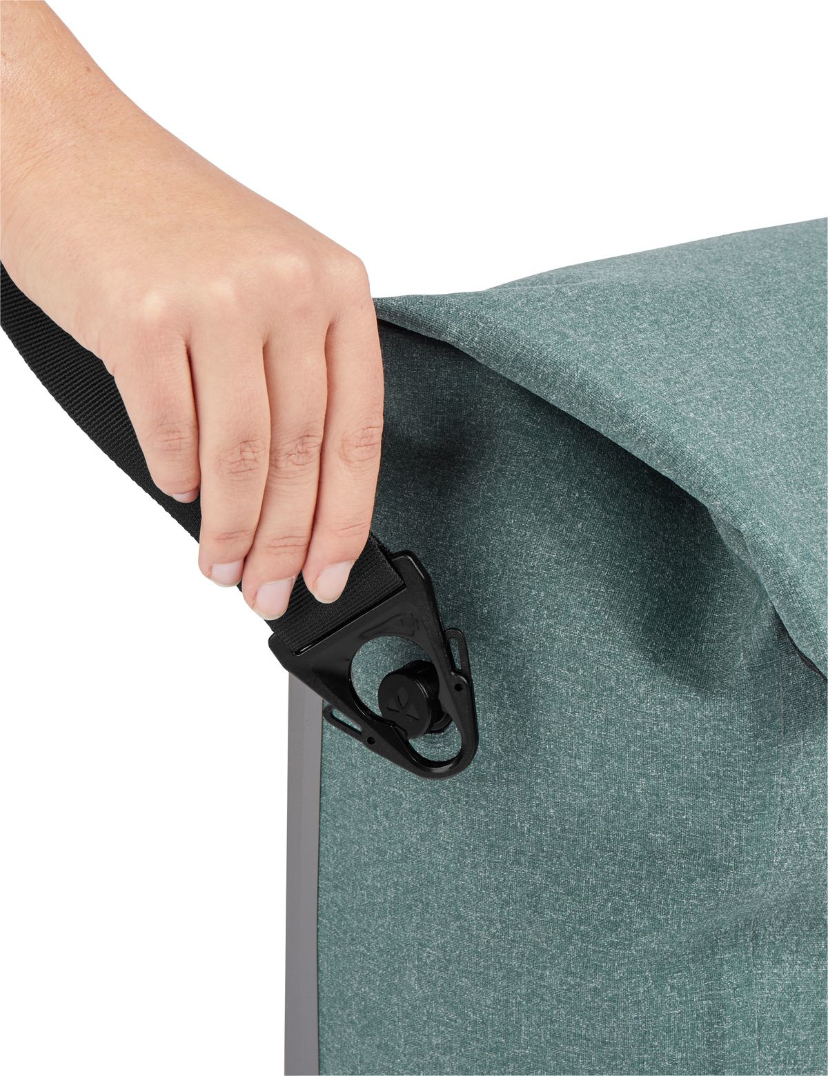 Eine Hand hält einen schwarzen Gurt, der mit einer tealfarbenen Stofftasche mit schwarzem Verschluss verbunden ist.