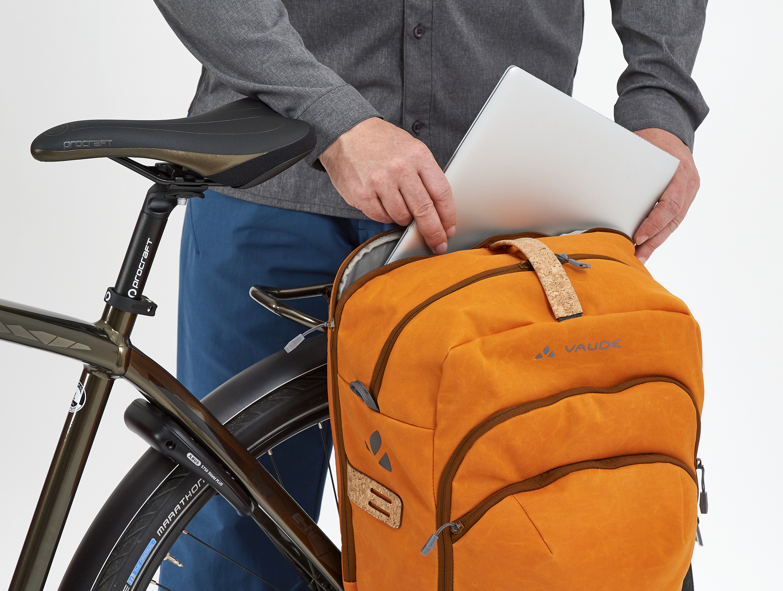Ein Mann, der einen Laptop in eine orangefarbene Fahrradtasche an einem Fahrrad steckt. Das Fahrrad ist braun.