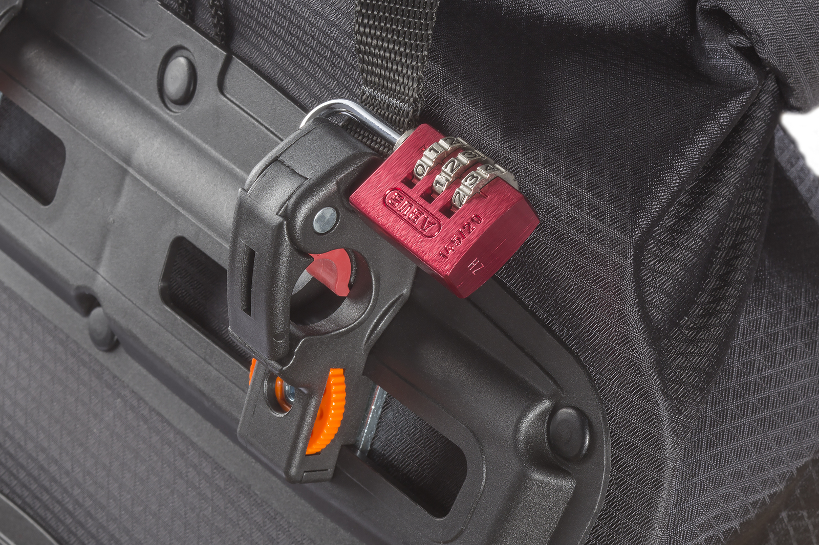 Czerwona kłódka szyfrowa na czarnej torbie rowerowej na białym tle.