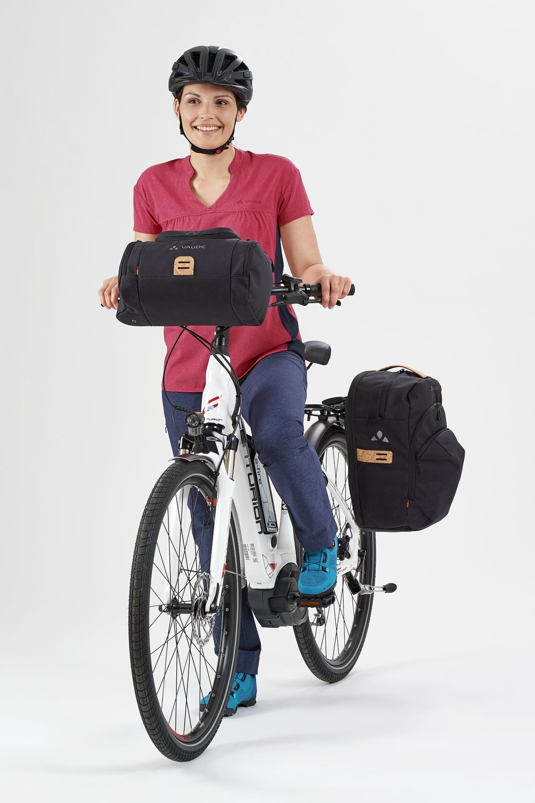 Frau fährt Fahrrad mit schwarzen Packtaschen, Helm und rotem Oberteil.