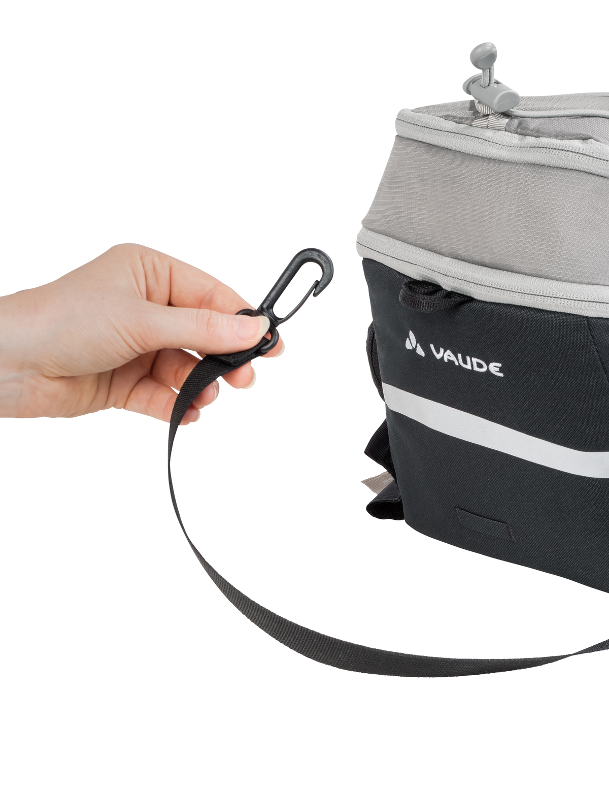 Person befestigt einen Gurt an einem Vaude Rucksack. Weißer Streifen und Vaude Logo sichtbar.