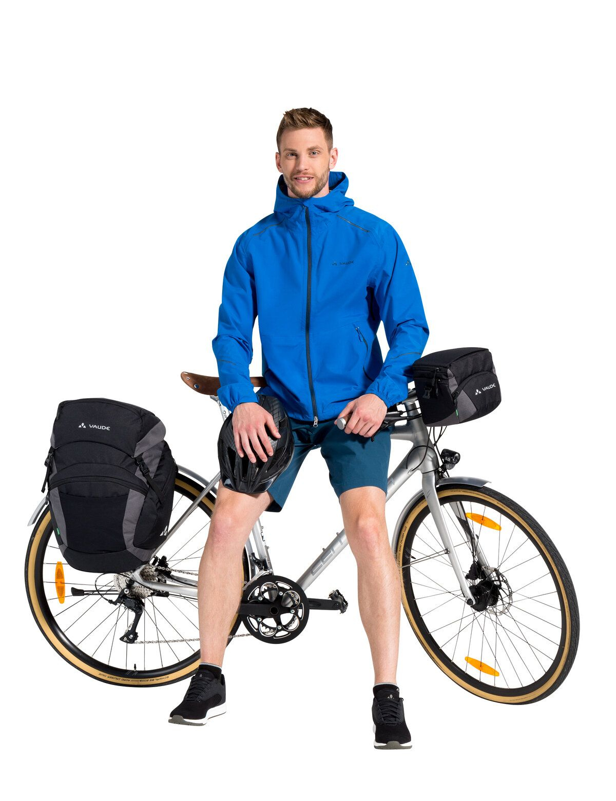Mann in blauer Jacke und Shorts mit Fahrrad und Taschen auf weißem Grund.