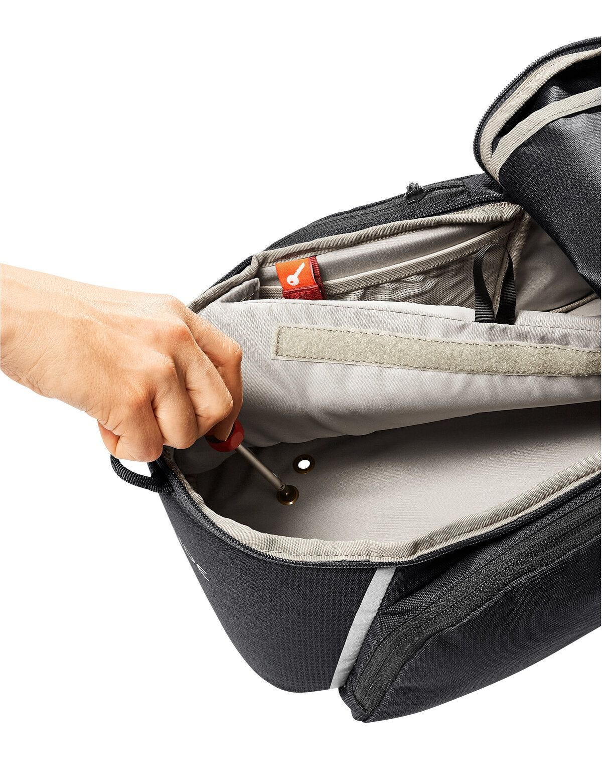 Ręka używająca śrubokręta do pracy wewnątrz czarnej torby.