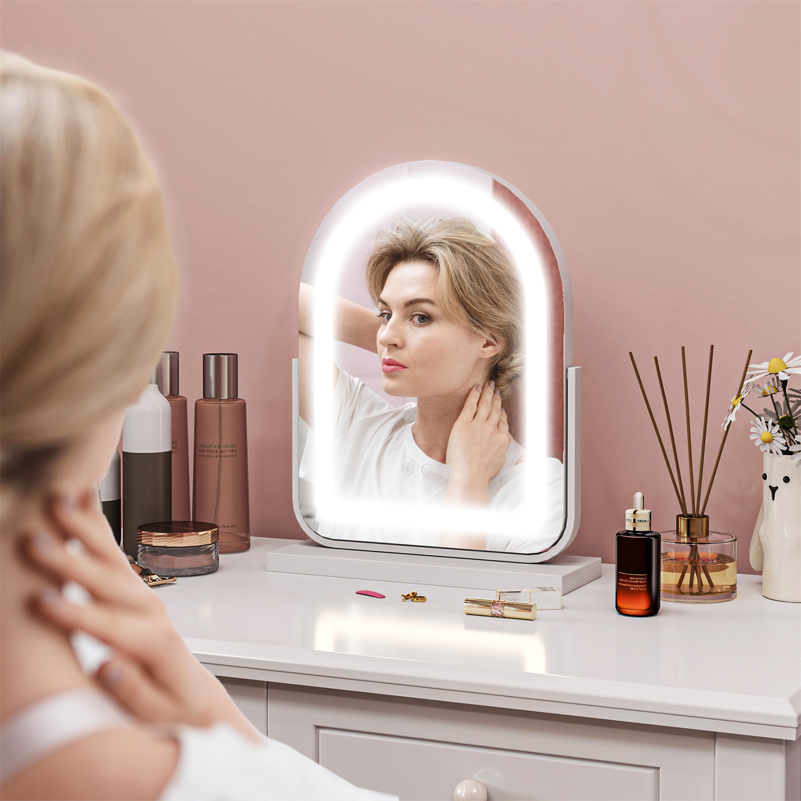 Frau im Spiegel, weißer Schminktisch. Spiegel mit Lichtern. Make-up auf dem Tisch. Rosa Wandhintergrund.