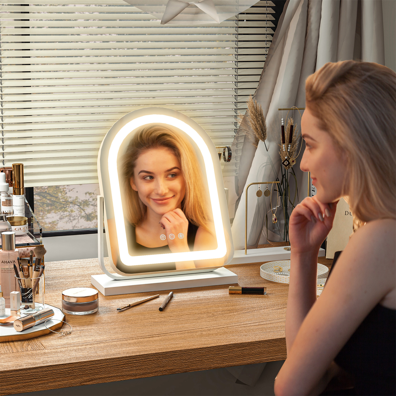 Eine Frau betrachtet sich in einem beleuchteten Schminkspiegel auf einem Holzschreibtisch, mit Make-up-Artikeln.
