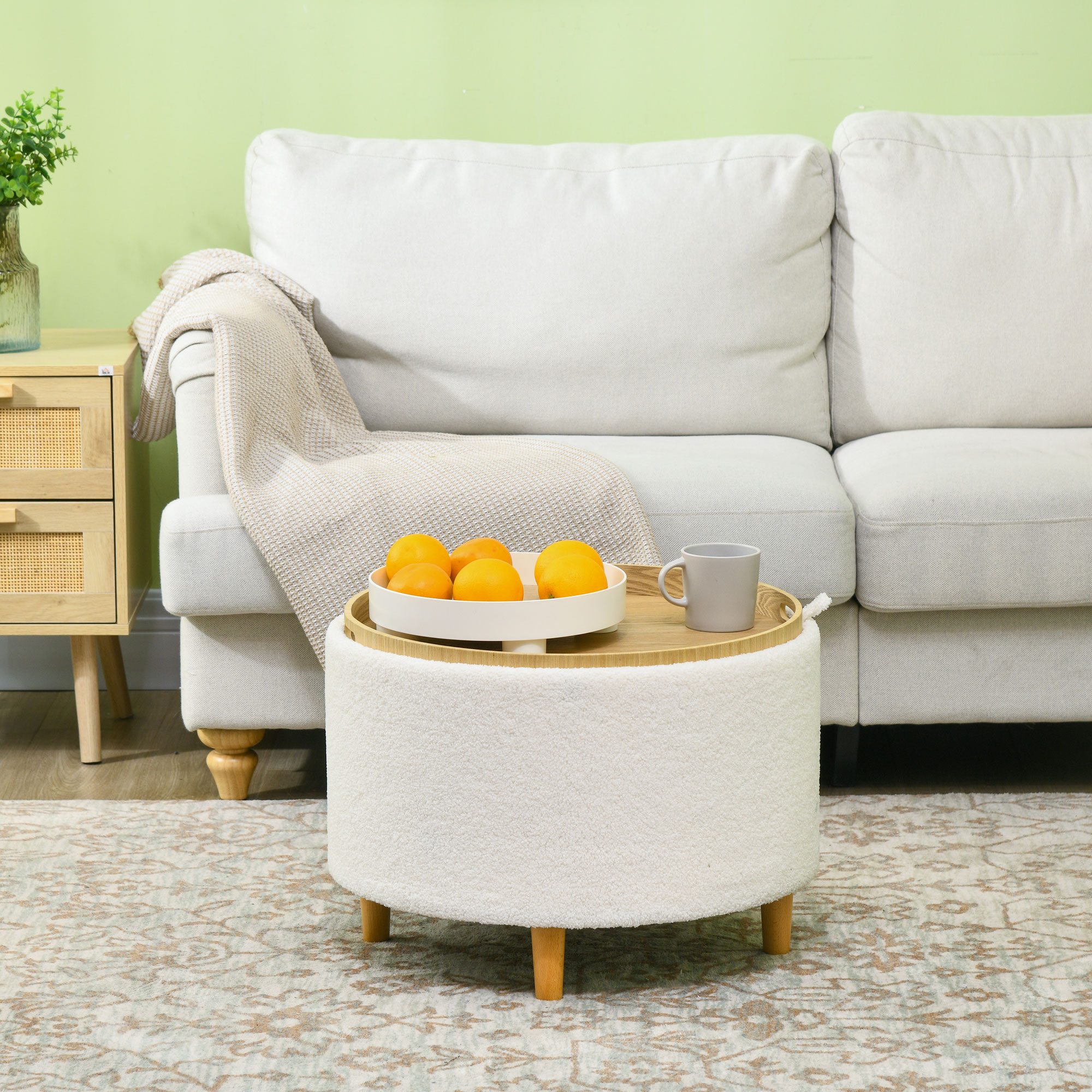 Ein weißer Hocker mit einer Schale Orangen und einer Tasse steht vor einem weißen Sofa.