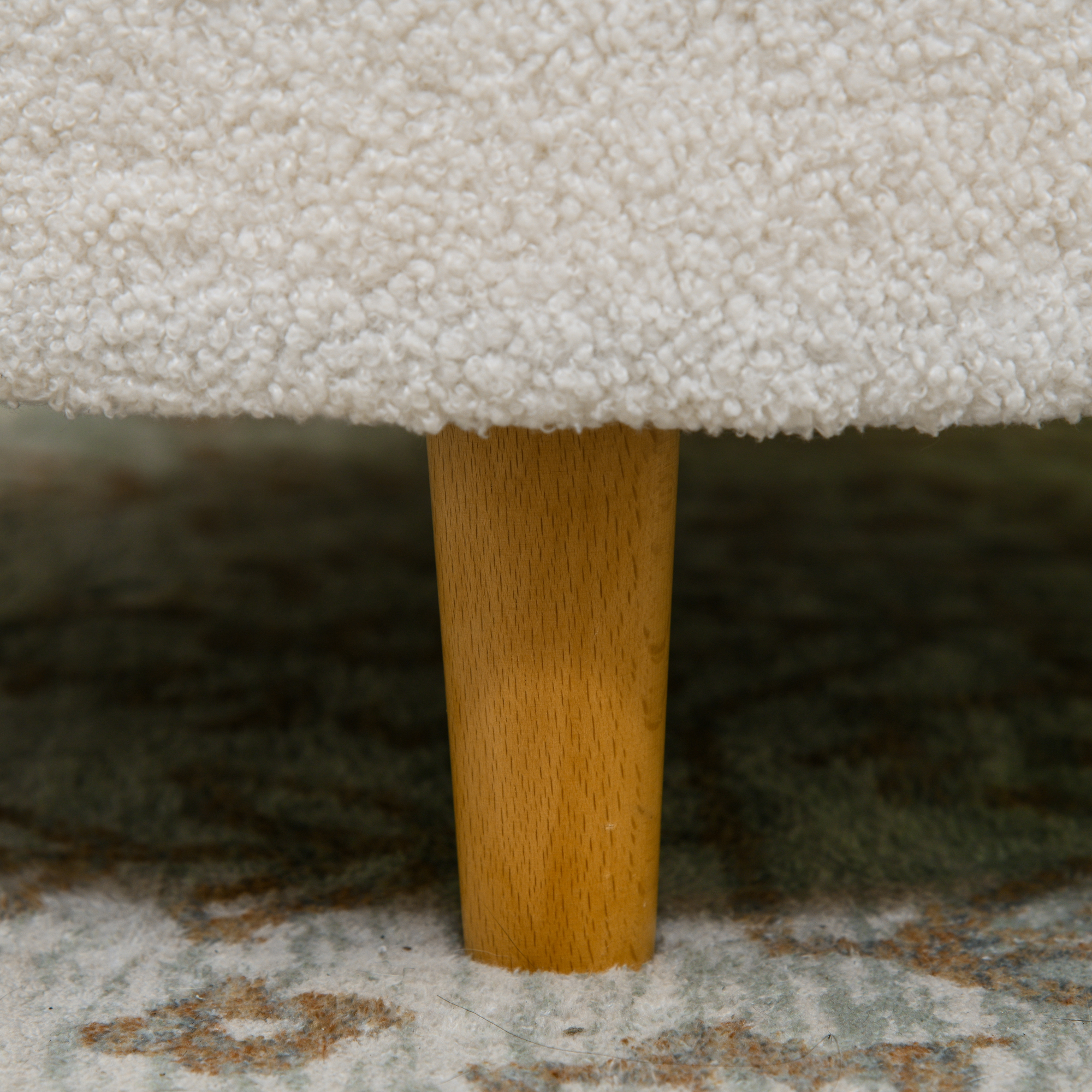 Nahaufnahme eines Holzmöbelfußes auf einem gemusterten Teppich.