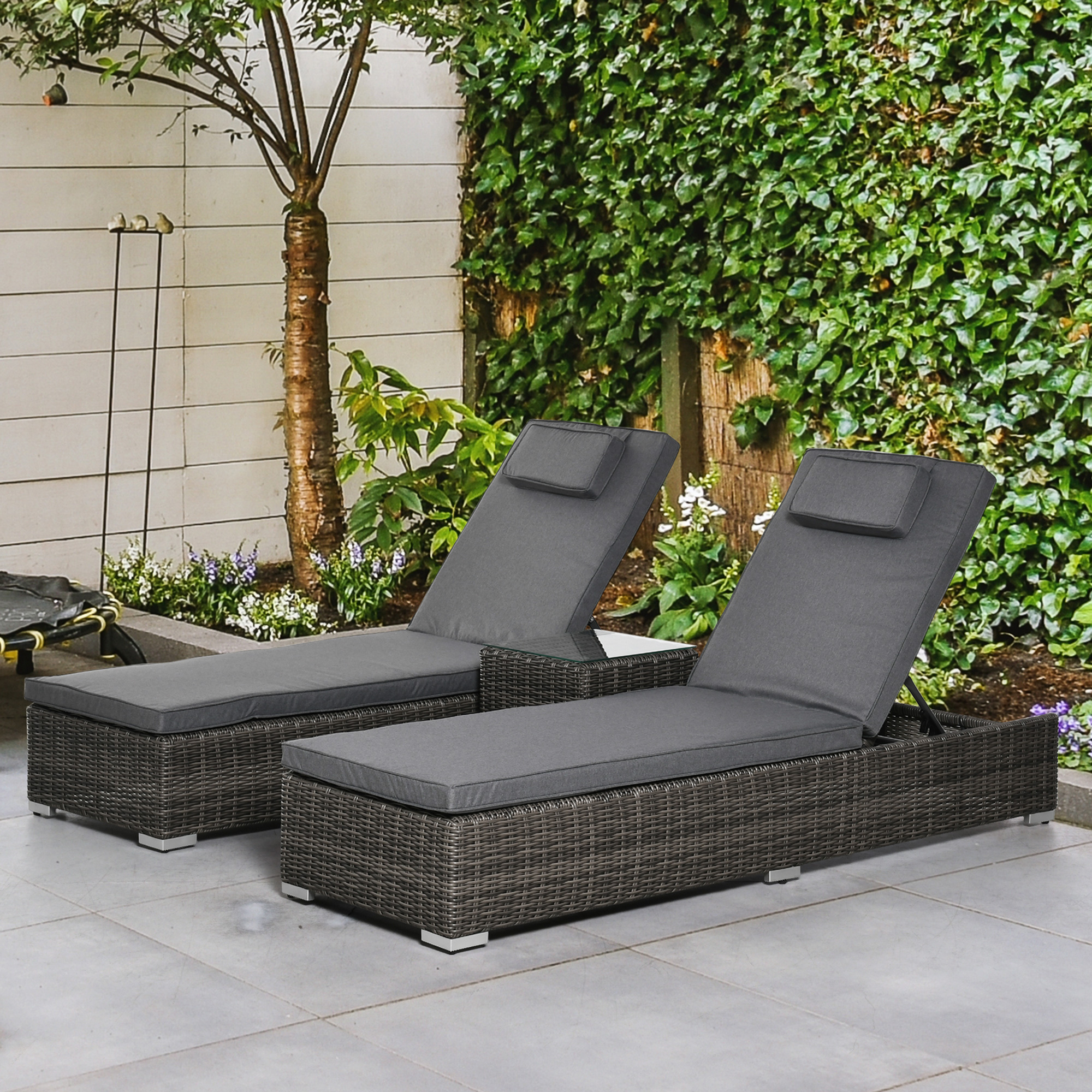 Zwei graue Outdoor-Liegestühle auf einer Terrasse, mit einer üppigen grünen Pflanzenwand im Hintergrund.