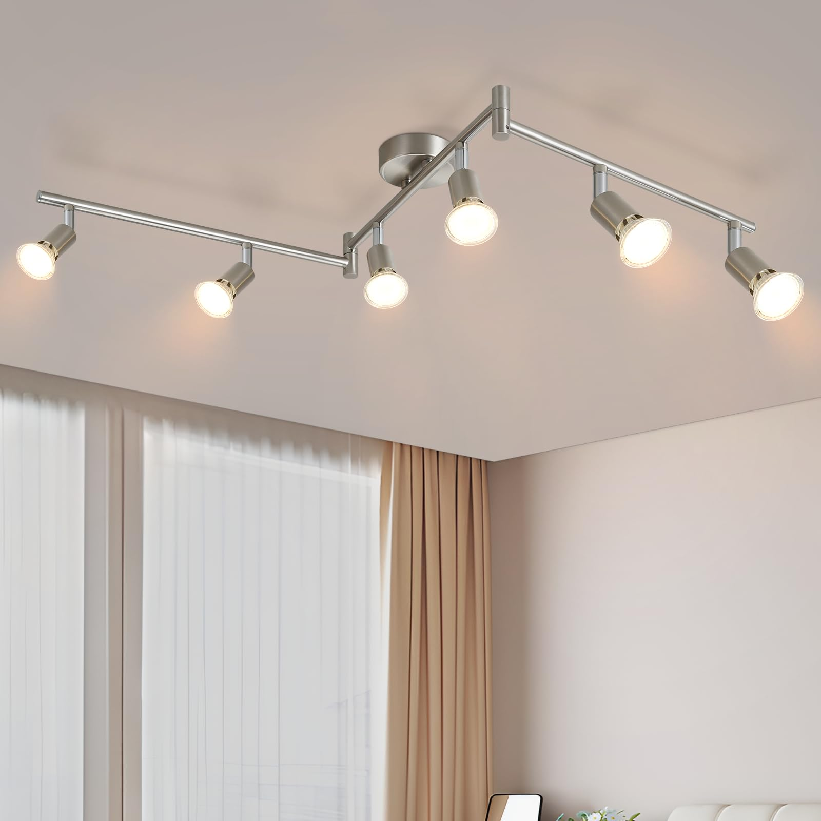 Eine an der Decke montierte Schienenbeleuchtung mit sechs Lichtern. Die Lichter sind silberfarben mit warmem Schein. Weiße Decke und Wand.