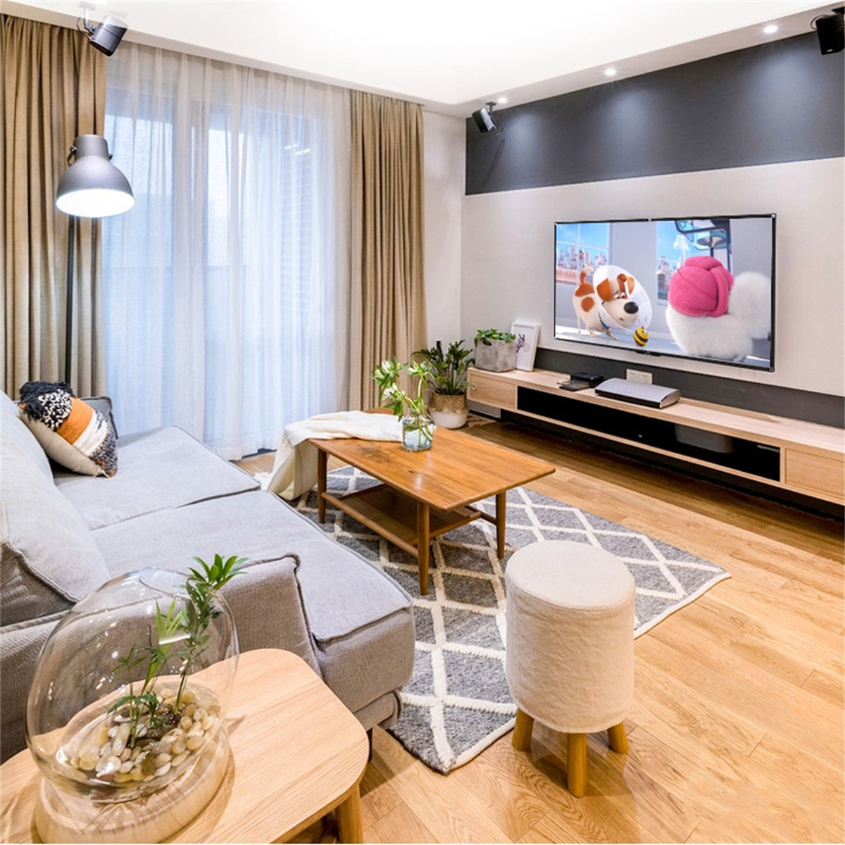 Wohnzimmer mit Sofa, Fernseher und Pflanzen. Graue Wände, Holzboden. Zeigt einen Cartoon im Fernsehen.
