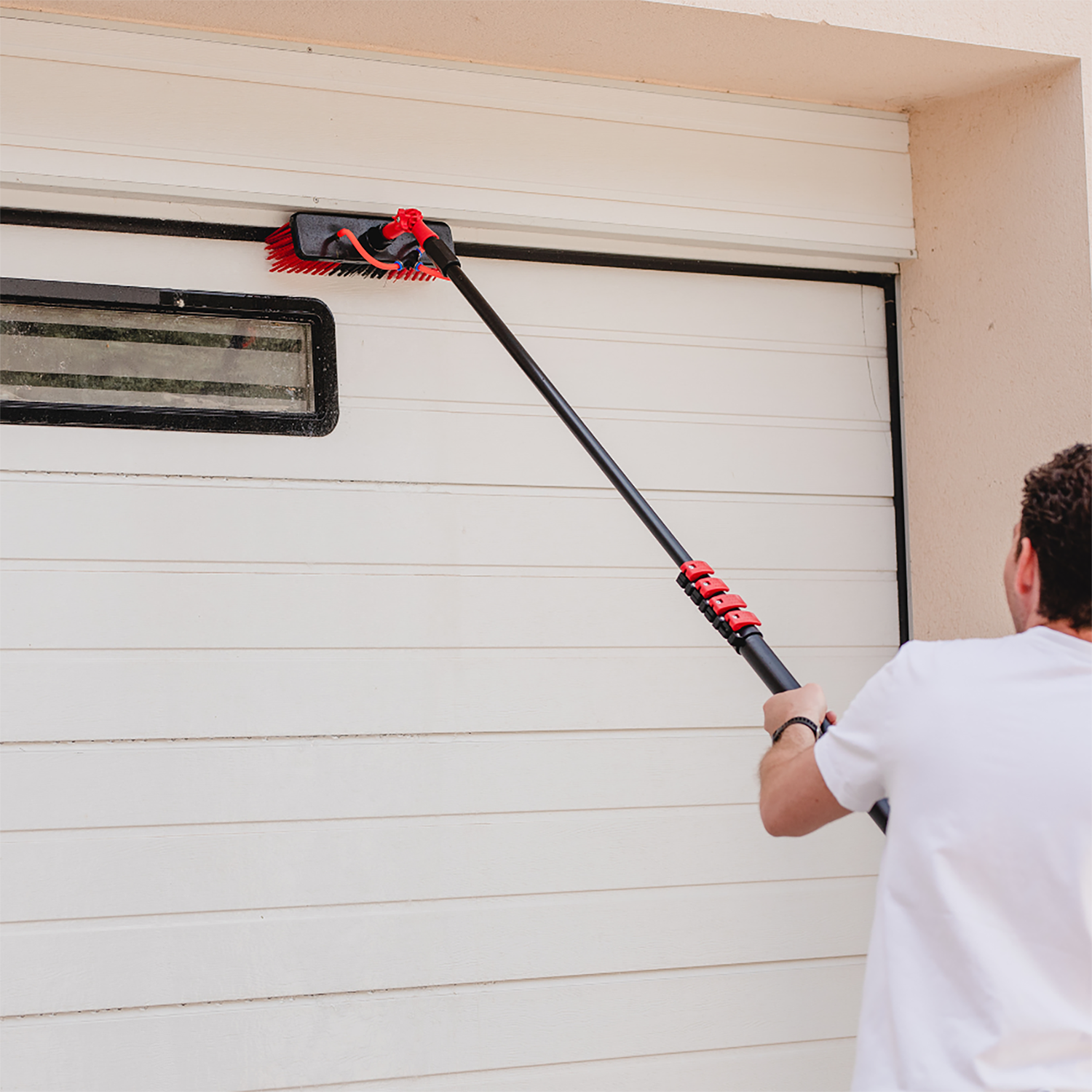 Man met een borstel met lange steel een witte garagedeur schoon. Zwarte borstel en steel.