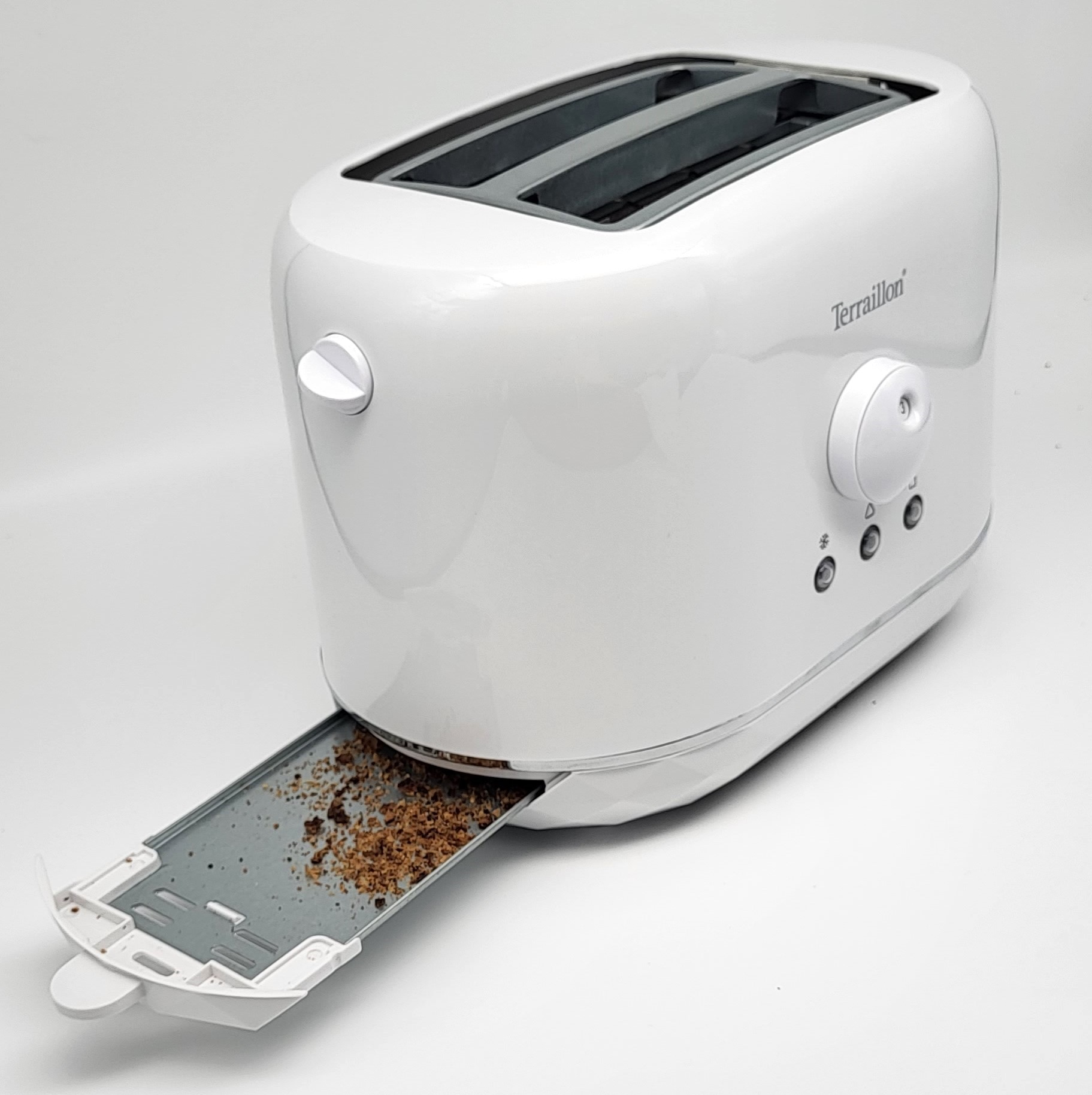 Biały toster z wysuniętą tacką na okruchy, pokazujący okruchy.