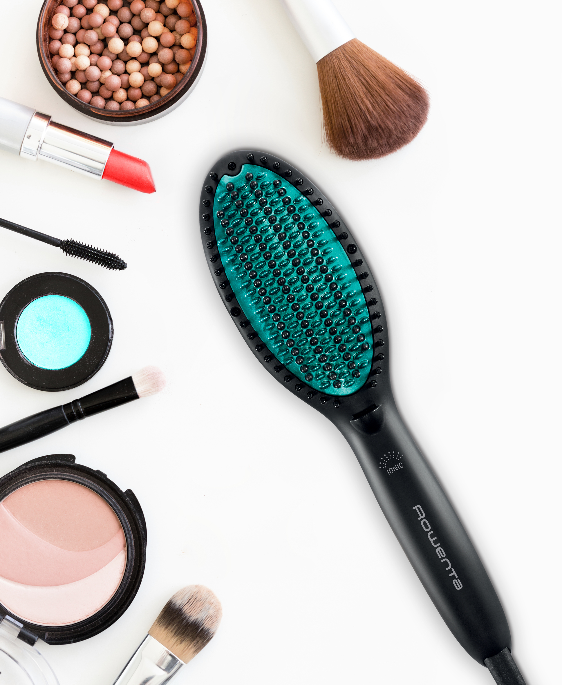 Makeup arrangement on white. Includes mascara, lipstick, brushes, and a hair straightener.