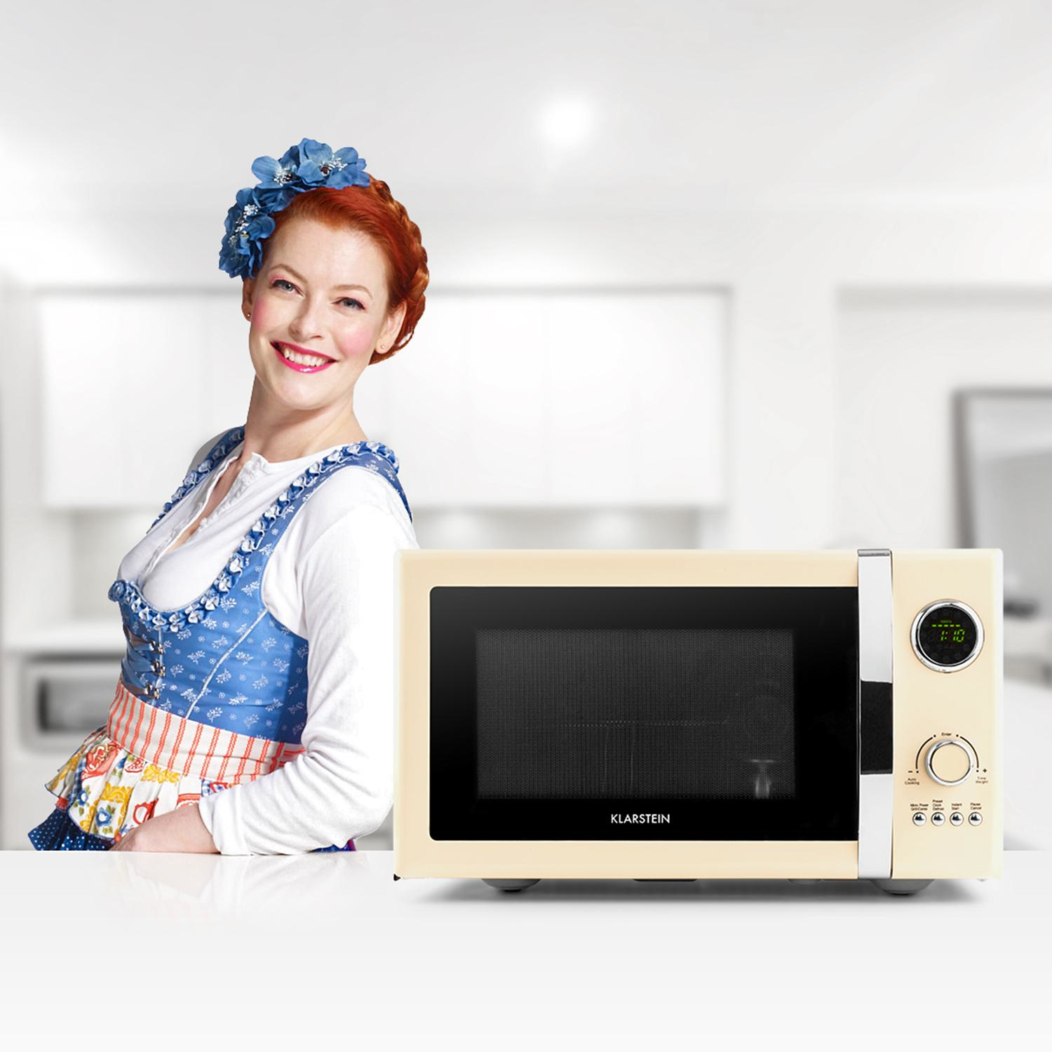Mujer con vestido bávaro tradicional con un horno microondas beige, sonriendo a la cámara.