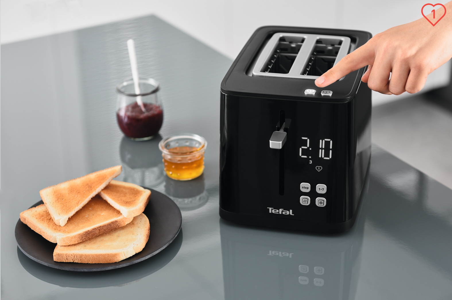 Czarny toster z tostami i dżemem na stole. Ręka naciska przycisk.