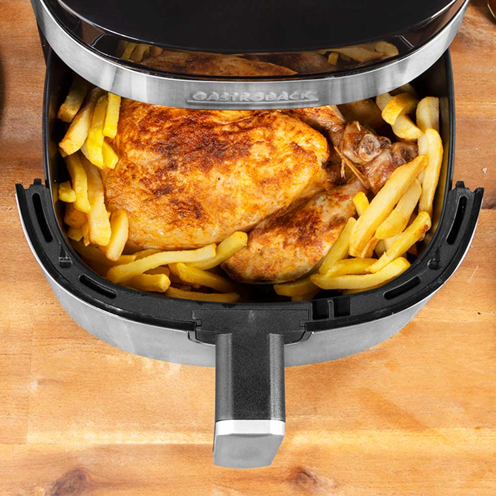 Friggitrice ad aria con pollo cotto e patatine fritte all'interno, su una superficie di legno.
