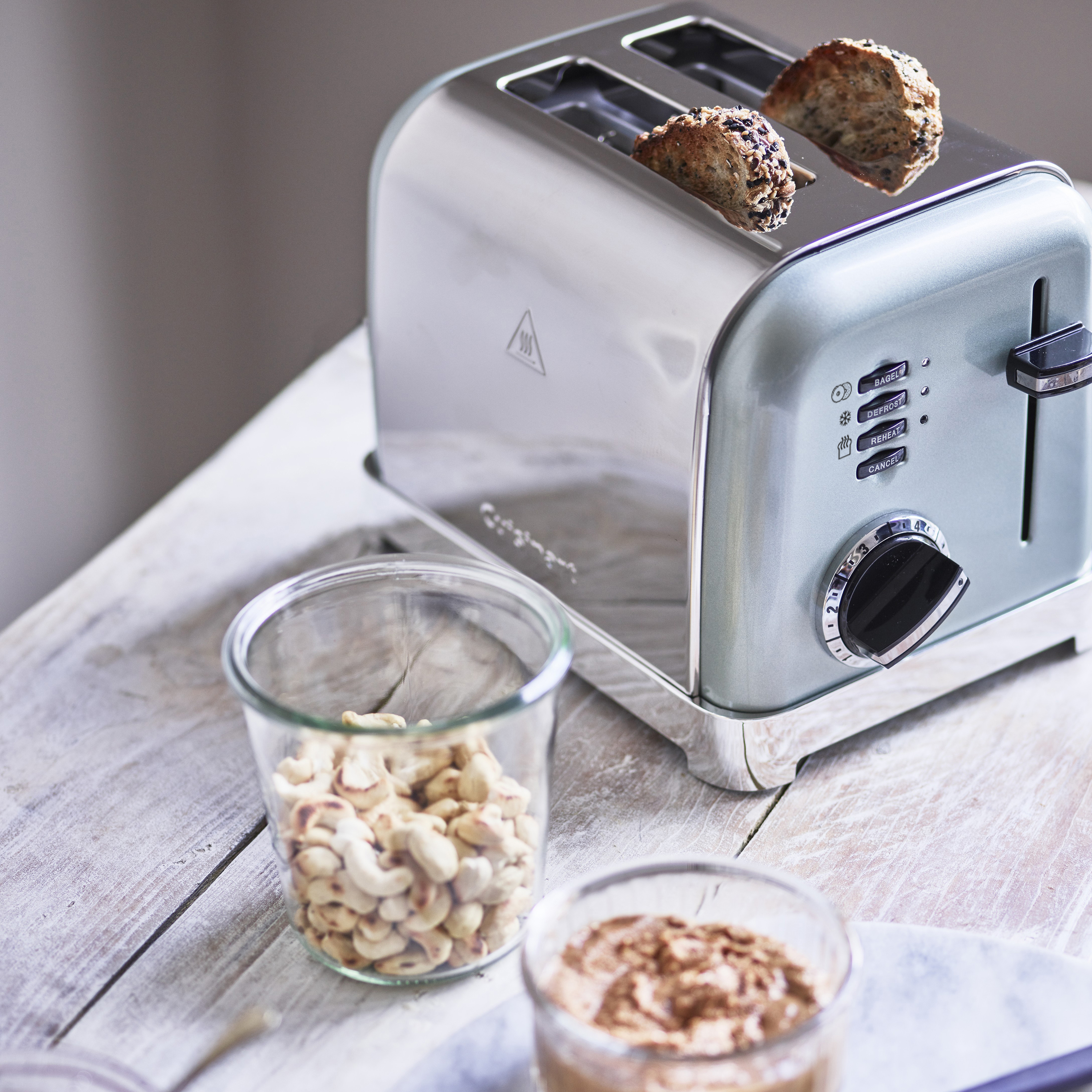 Srebrny toster z chlebem. Obecne są również orzechy nerkowca i deser w szklance.