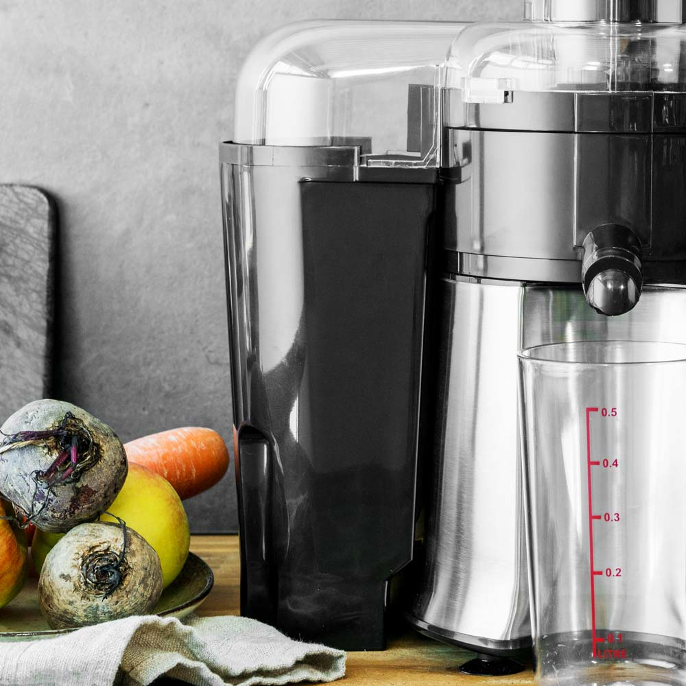 Estrattore di succo con barbabietole, carote, mele e un bicchiere pieno di succo accanto a un misurino.