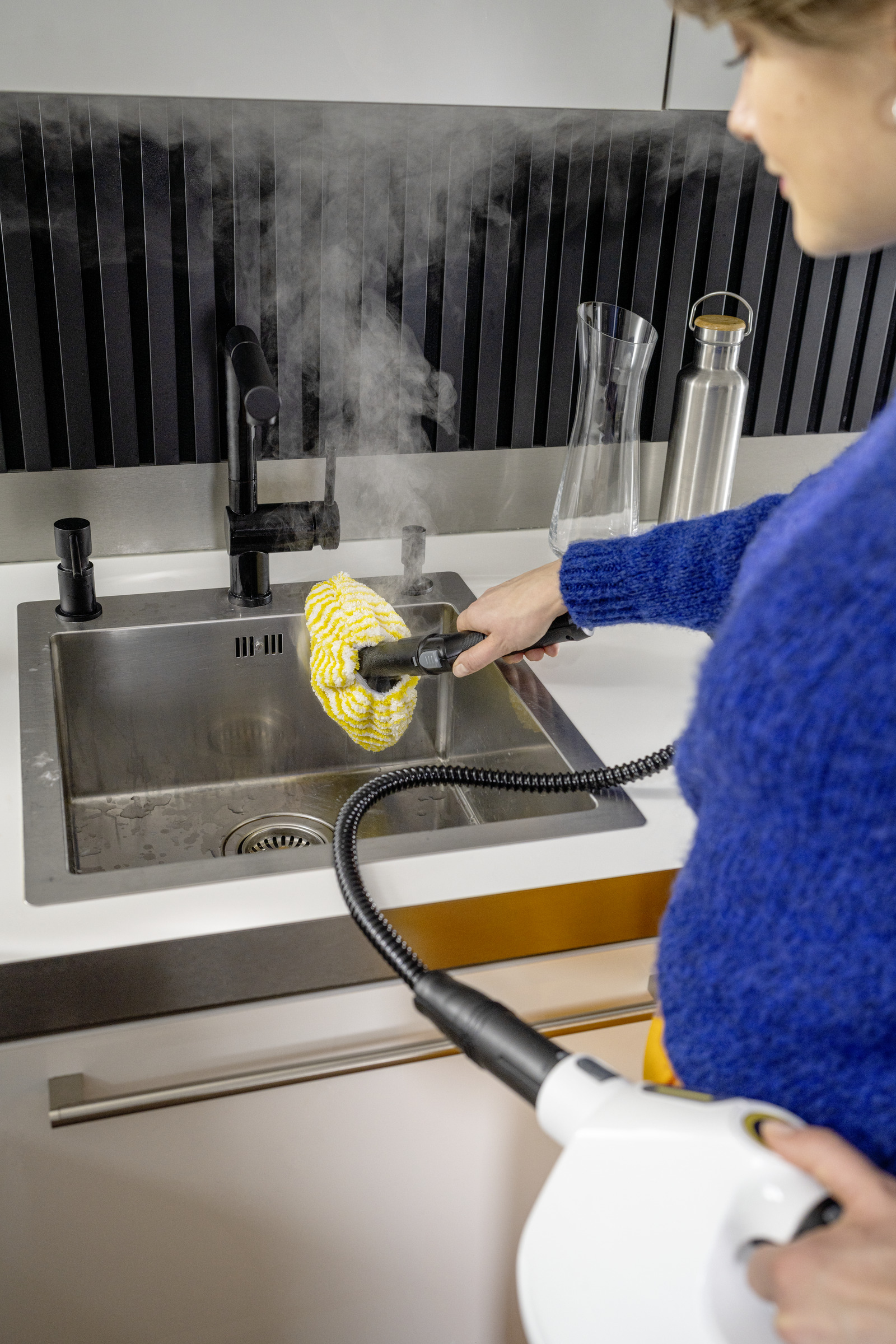 Kobieta paruje zlew parownicą ręczną. Para unosi się ze zlewu.