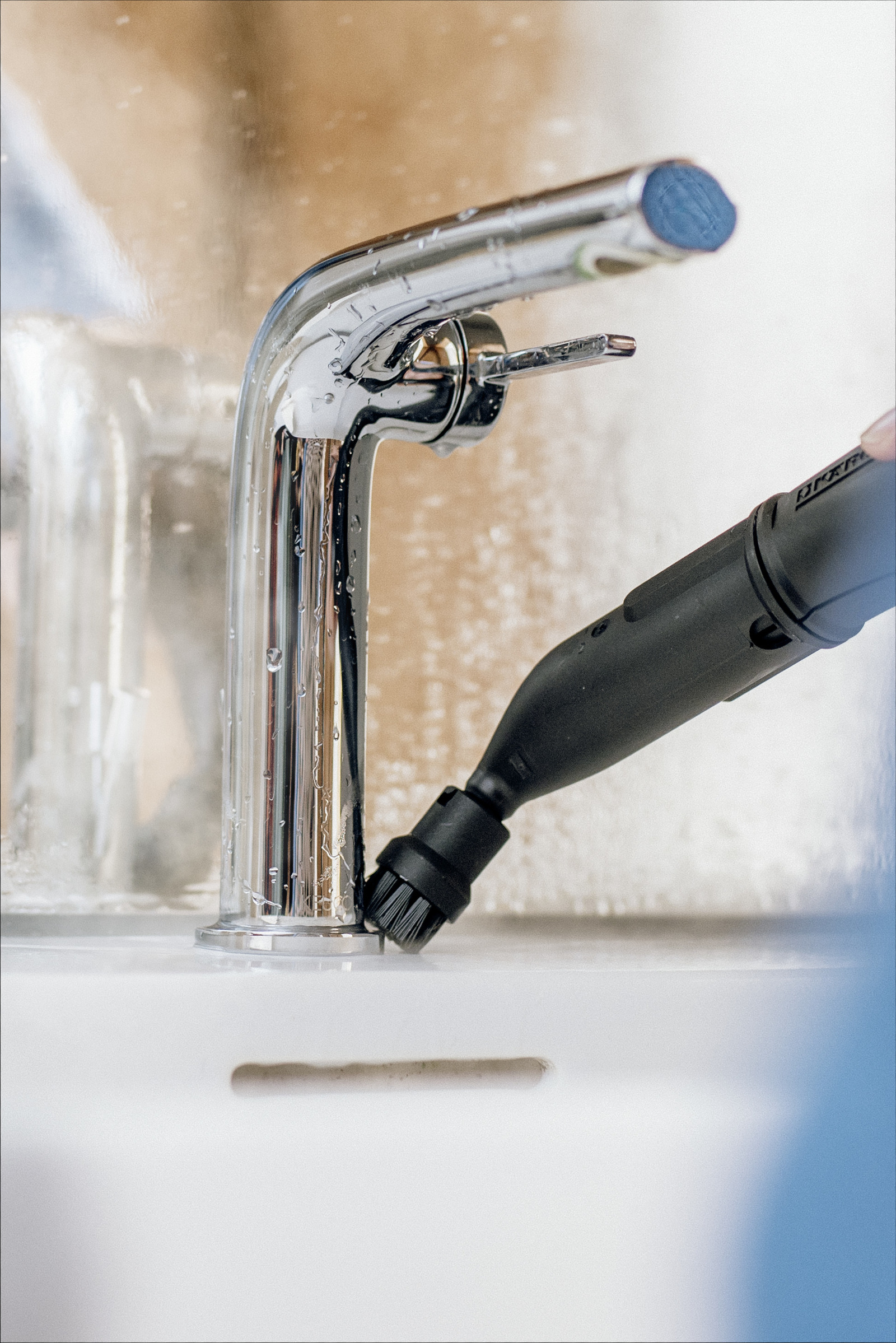 Chromowana bateria czyszczona parownicą. Widoczne krople wody. Zlew jest biały.