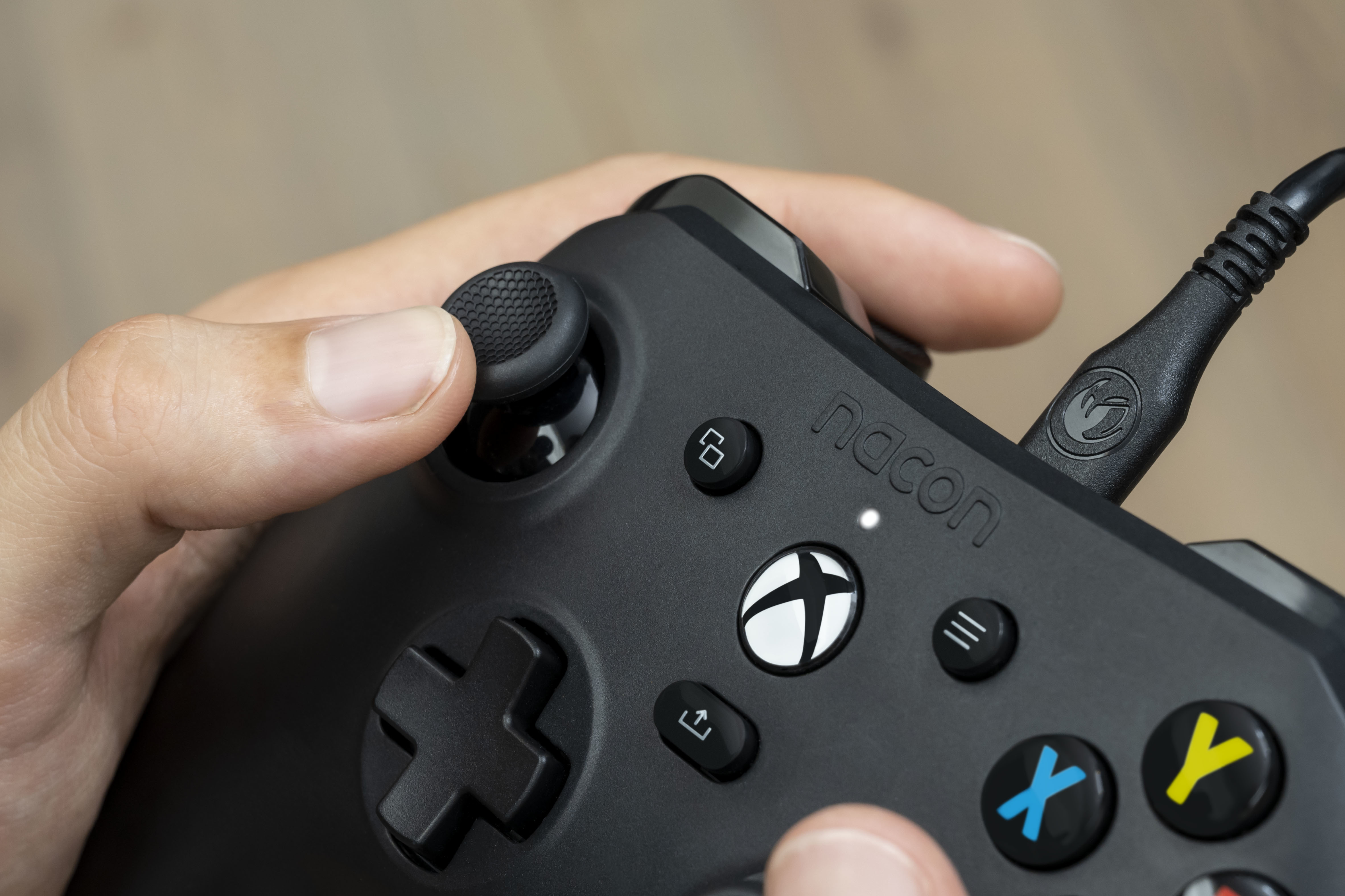 Dłoń trzymająca czarny kontroler Xbox. Kciuk jest na joysticku. Przyciski są widoczne.