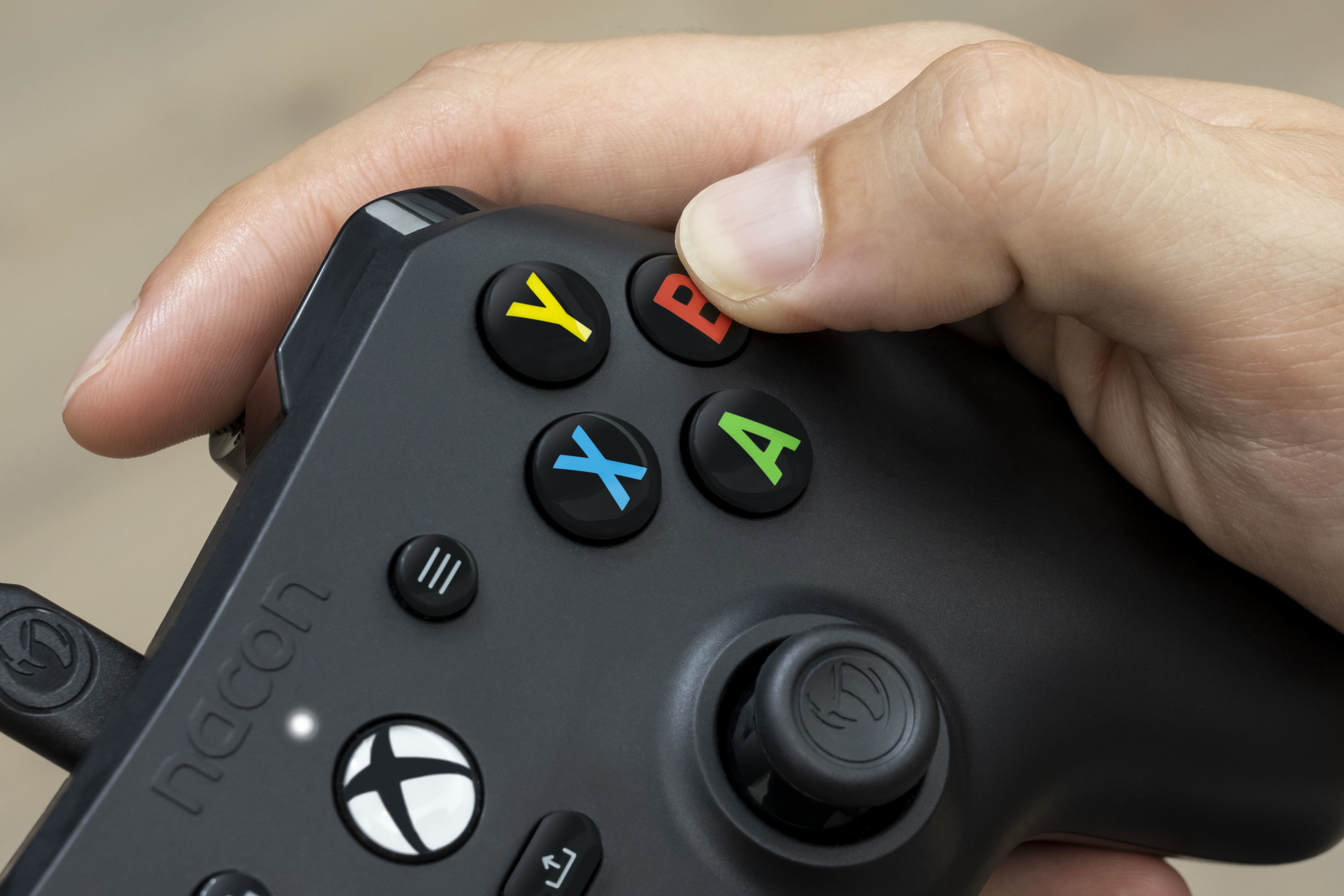 Dłoń trzymająca czarny kontroler do gier Hacon z kolorowymi przyciskami i joystickiem. Zbliżenie.