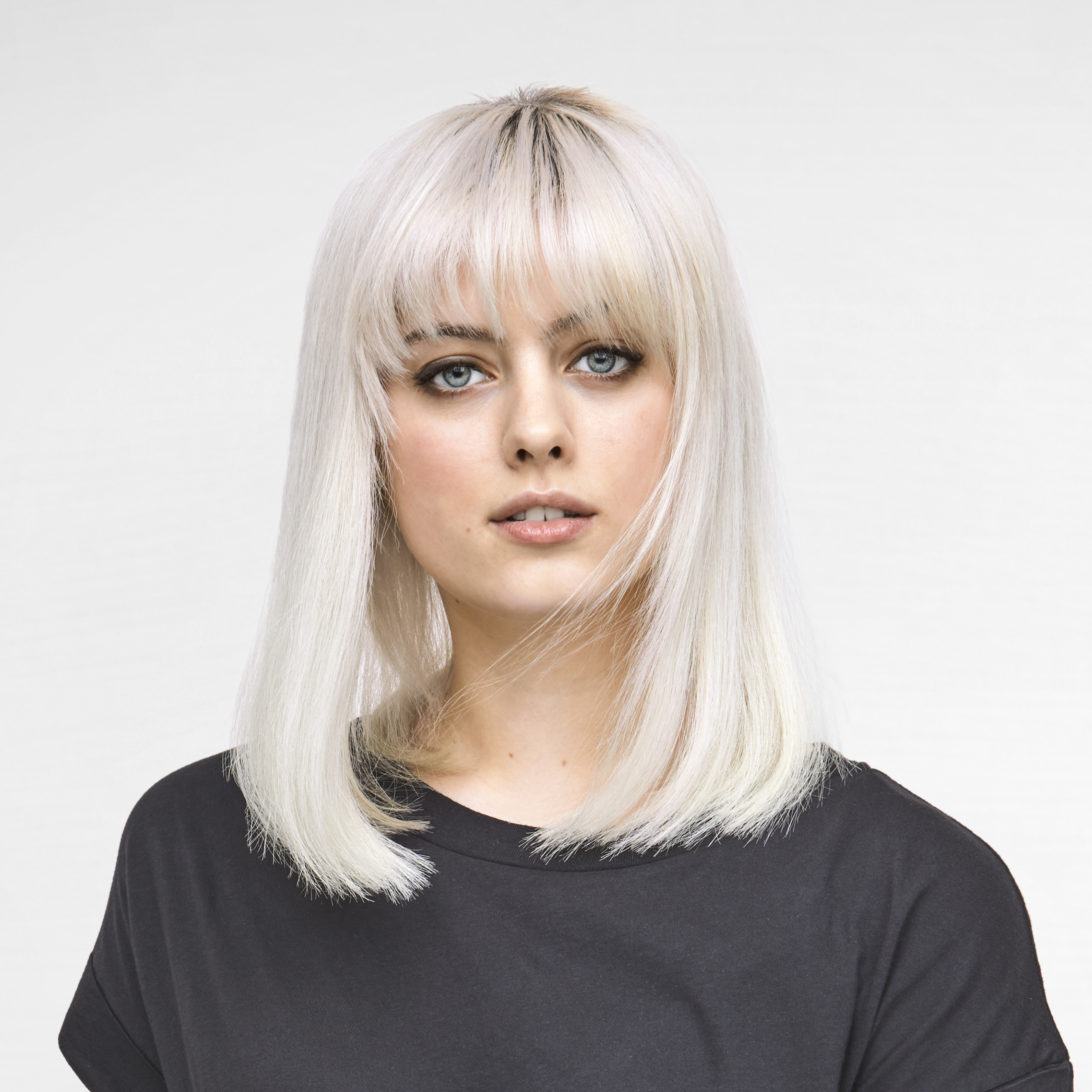 Kobieta z blond włosami i czarną koszulką patrzy w kamerę. Jej włosy zakrywają czoło.