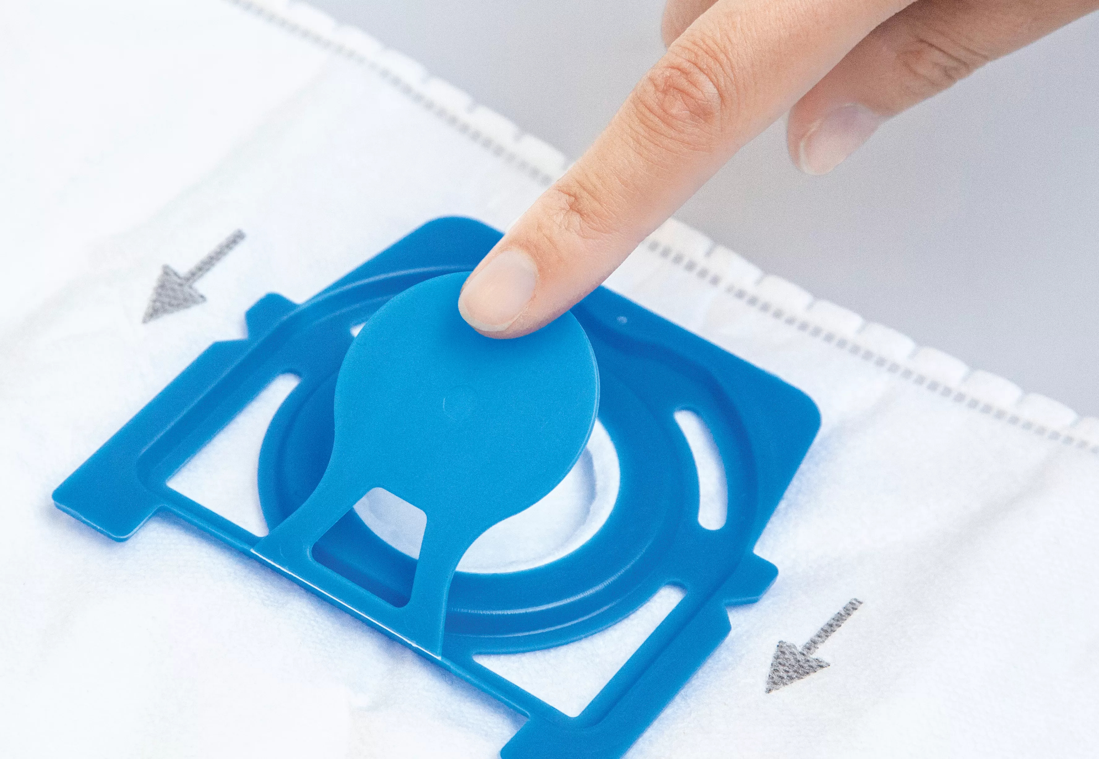 Un dito preme la chiusura blu su un sacchetto aspirapolvere bianco.