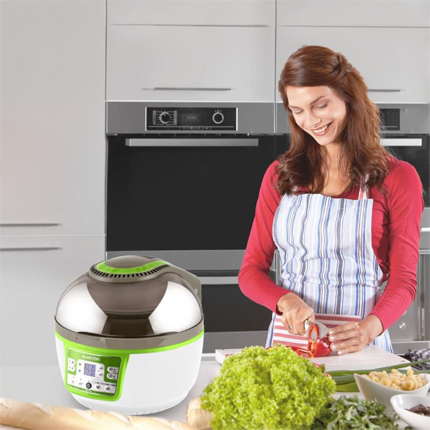 Una donna taglia un peperone rosso vicino a una friggitrice ad aria con un pannello verde, in una cucina.