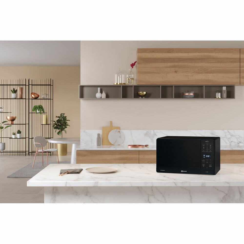 Schwarze Mikrowelle auf einer Küchenzeile. Küche hat Holzschrank und Marmortisch.