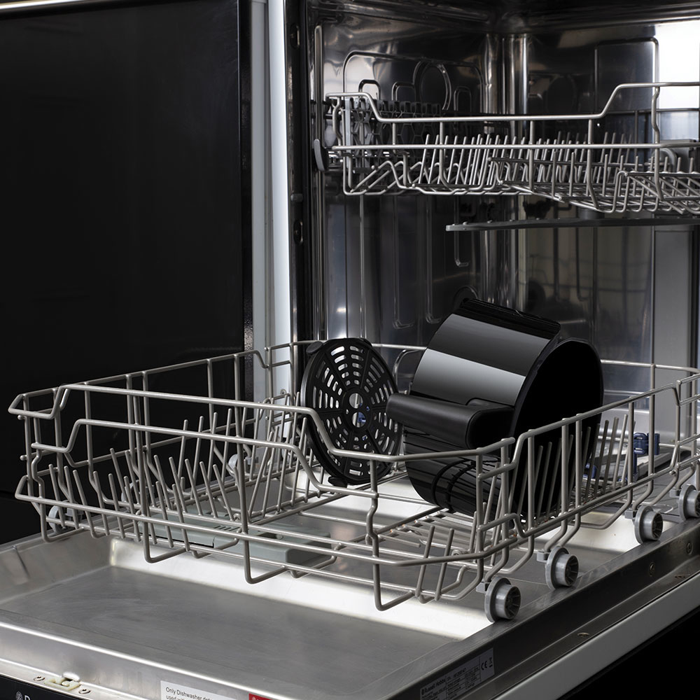 Lavastoviglie aperta. Interno con ripiani e un cestello per friggitrice ad aria nero. Colori metallici e neri.