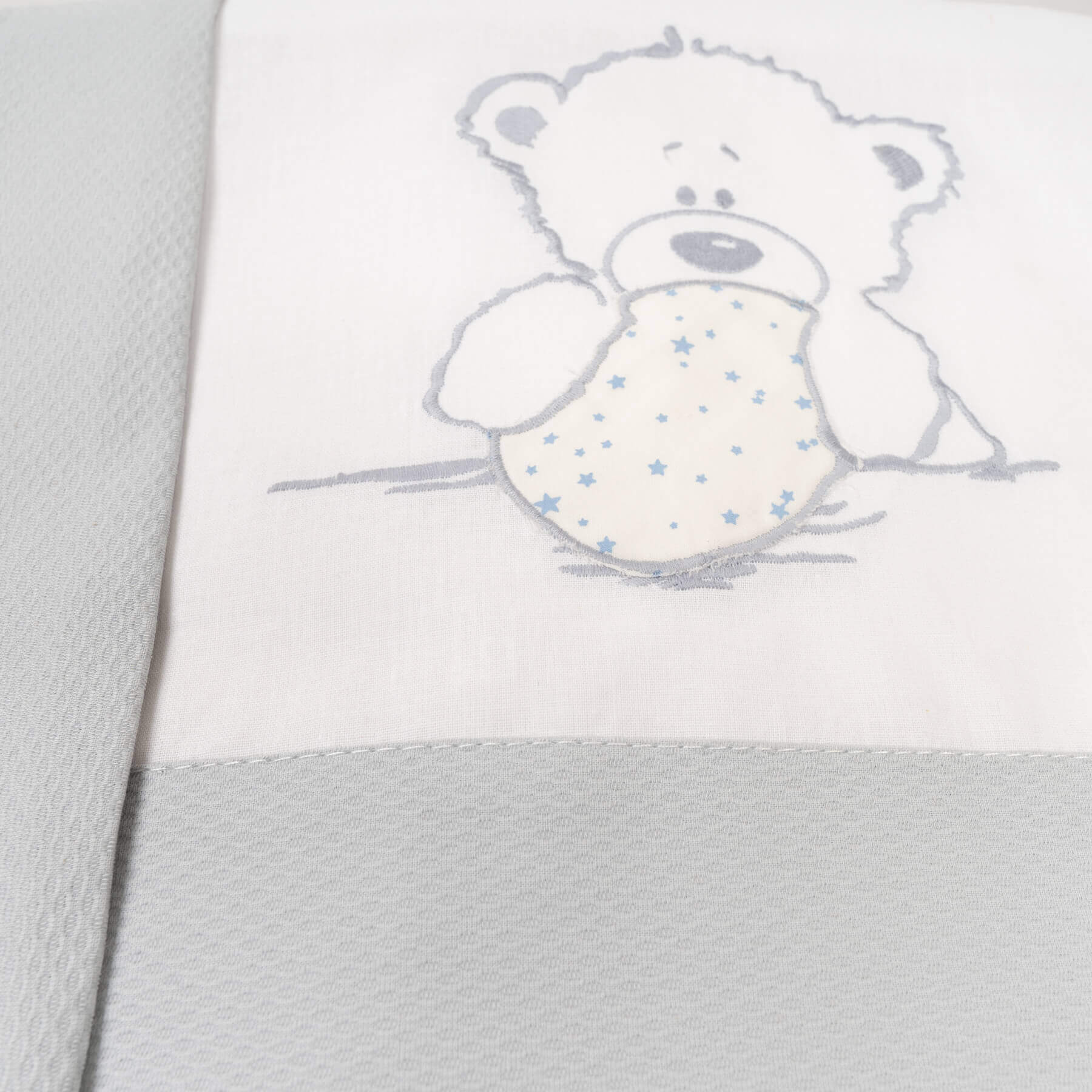Manta de bebé blanca con diseño de osito, acentos grises y patrón de estrellas.