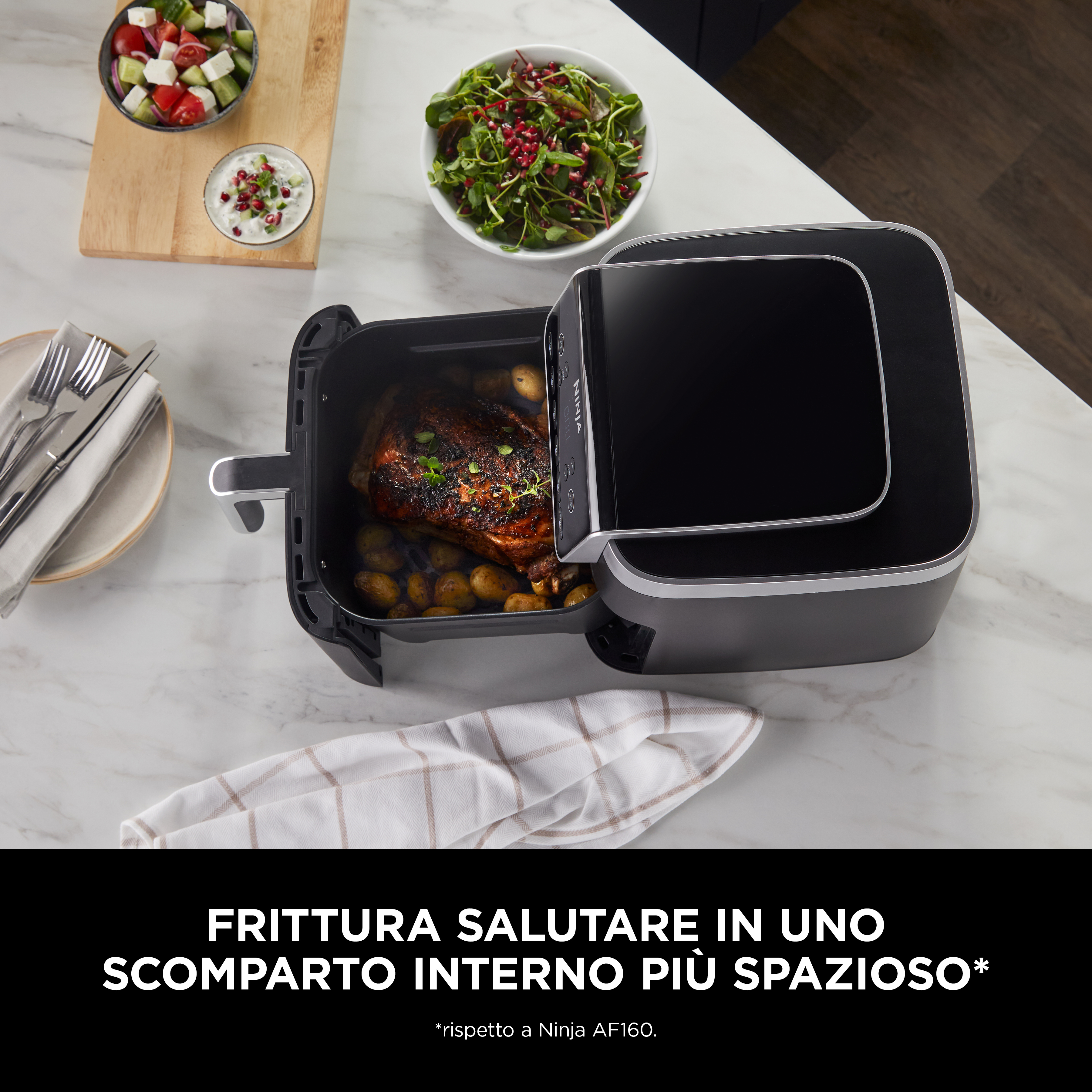 Friggitrice ad aria nera con cibo all'interno e un'insalata a lato, su una superficie di marmo.