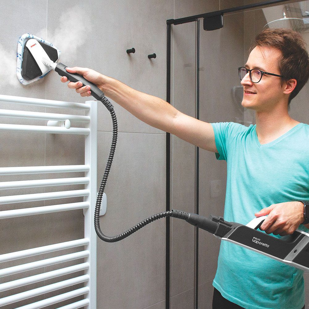 Mężczyzna używający parownicy na ścianie łazienki, w okularach i turkusowej koszuli.