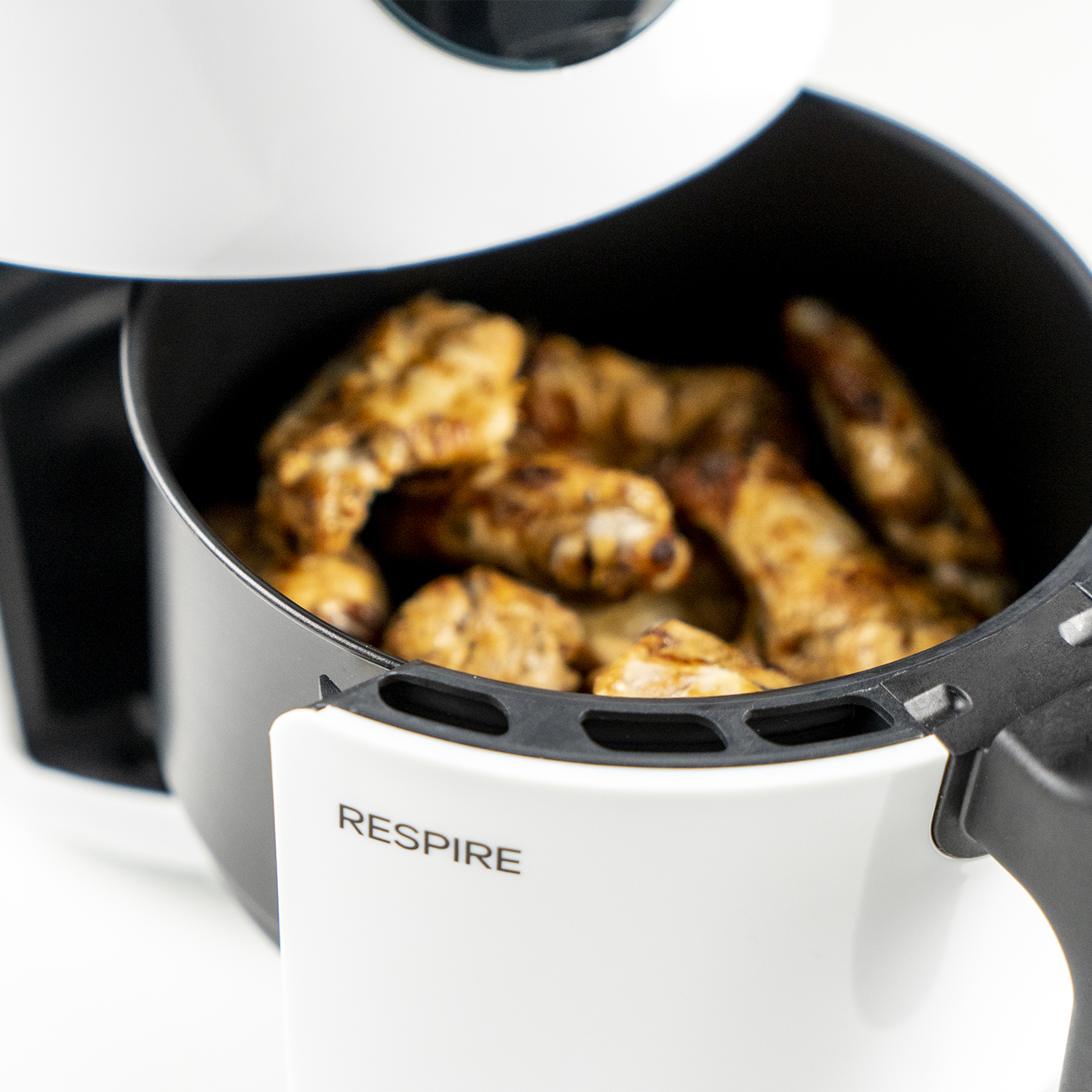 Freidora de aire con alitas de pollo cocinadas. Diseño blanco y negro. Visible la palabra "RESPIRE".