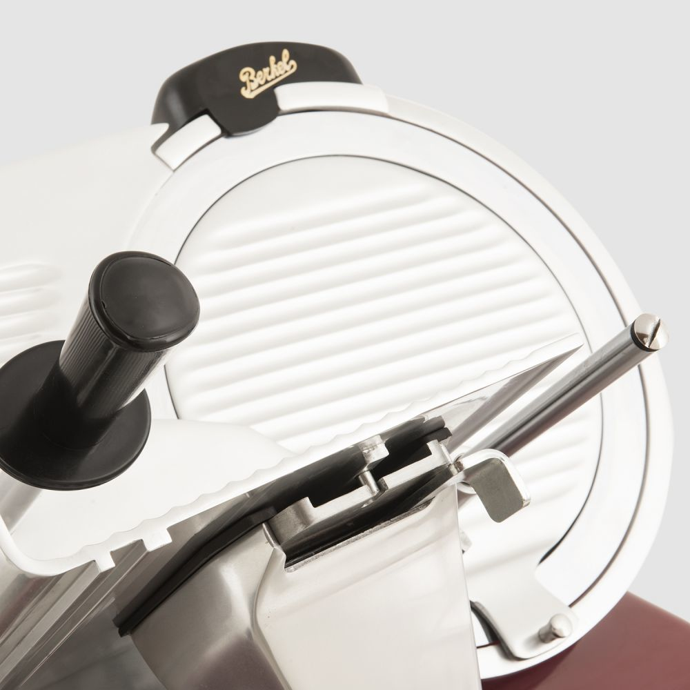 Zbliżenie krajalnicy do mięsa Berkel. Widoczne ostrze i uchwyt. Schemat kolorów biały i czerwony.