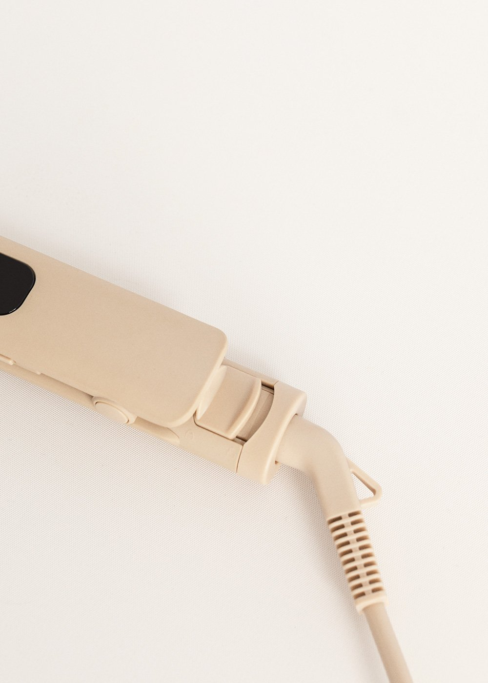 Plancha de pelo beige con cable y enchufe sobre un fondo blanco.