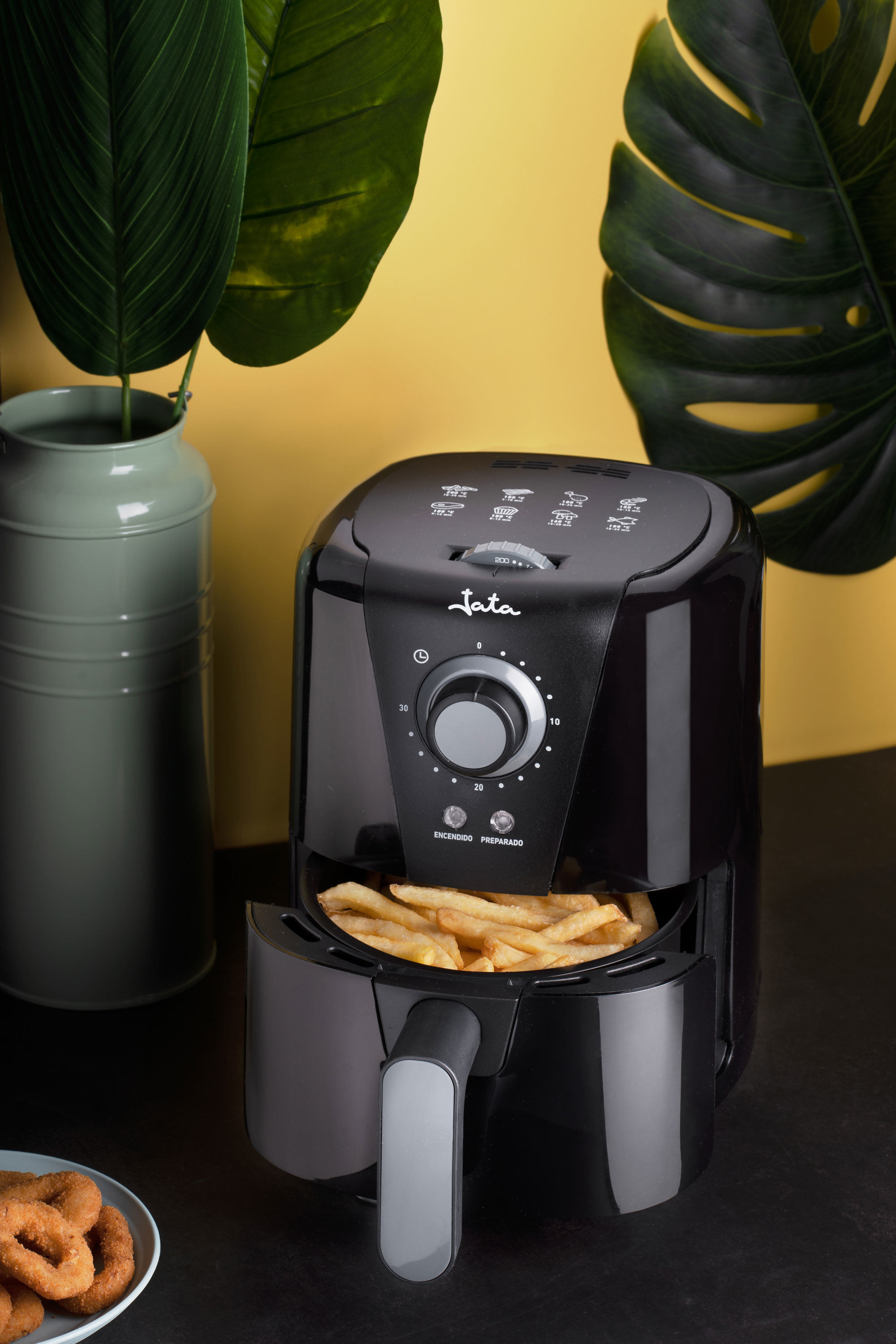 Friggitrice ad aria nera con patatine fritte, foglie e un muro dorato sullo sfondo.