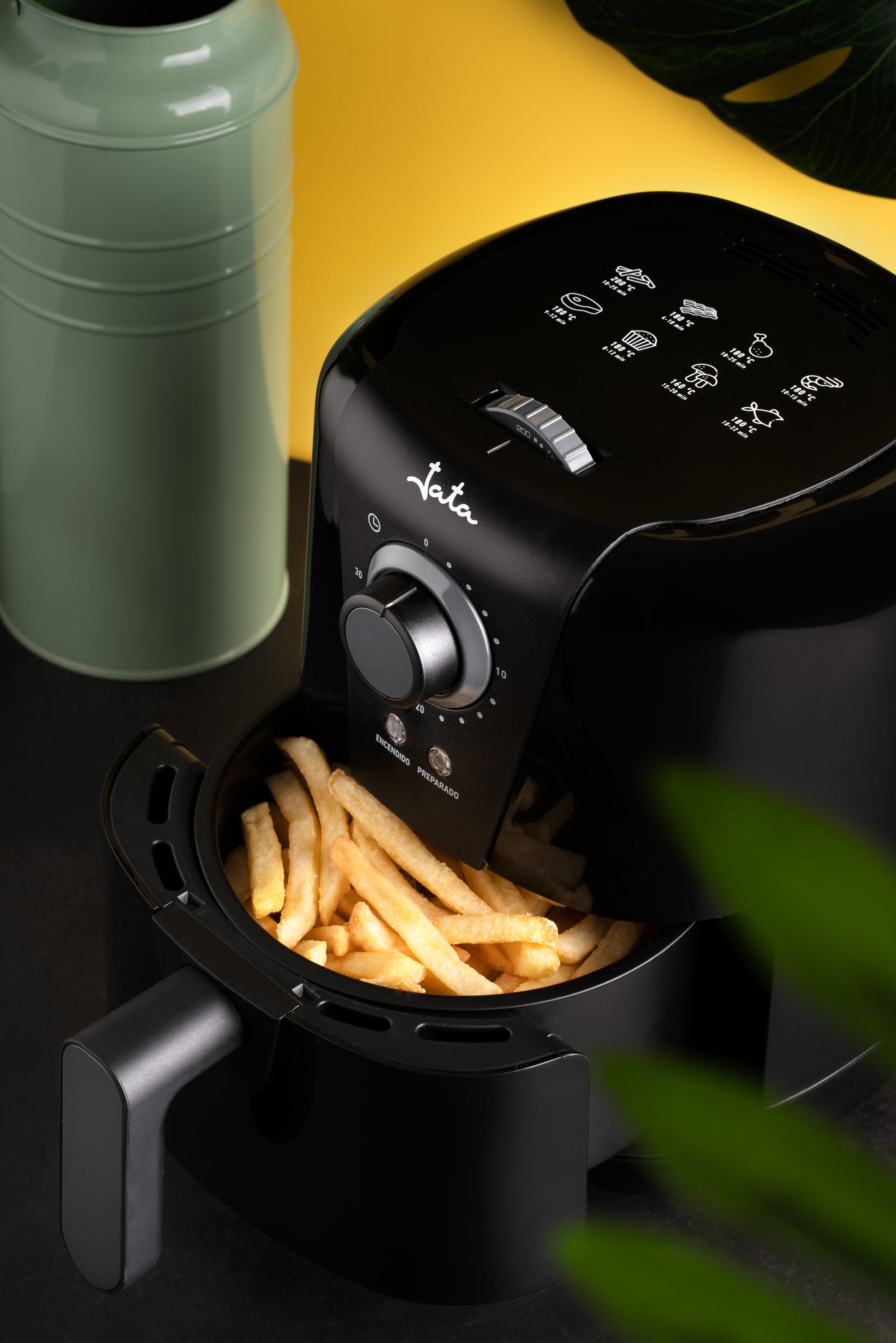 Friggitrice ad aria nera con patatine fritte. È su una superficie nera con sfondo verde e giallo.
