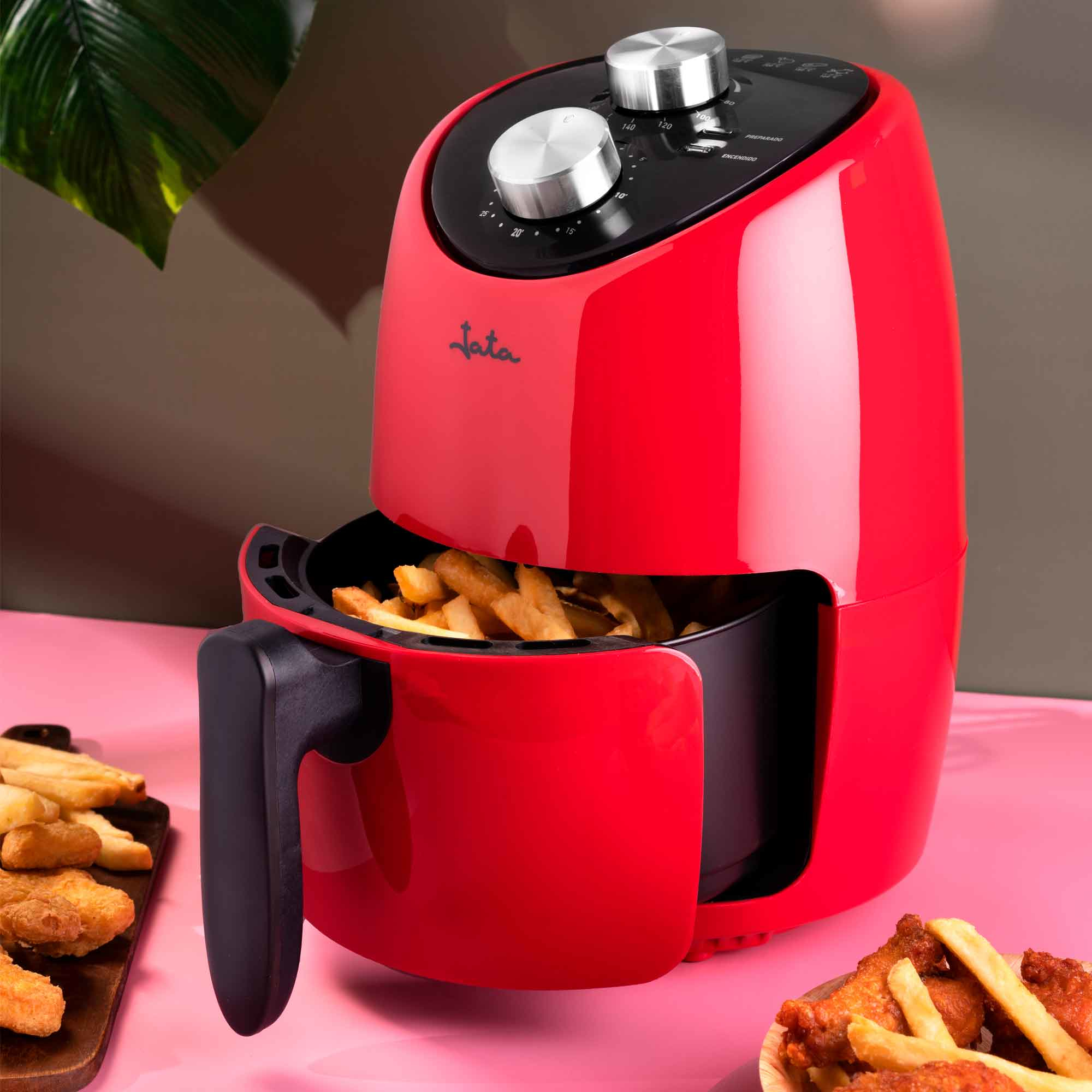 Freidora de aire roja con patatas fritas en la cesta. Superficie rosa, fondo marrón y rosa.
