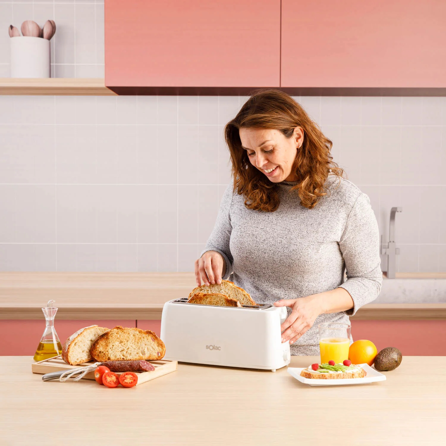 Kobieta wkładająca chleb do białego tostera. Produkty spożywcze na drewnianej powierzchni.