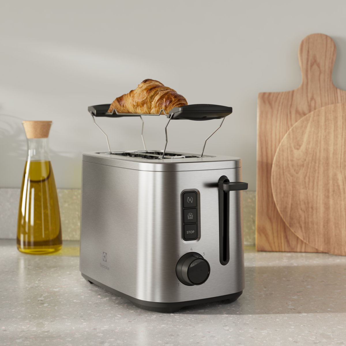 Toaster aus Edelstahl mit Croissant, Olivenölflasche und Holzbrett im Hintergrund.