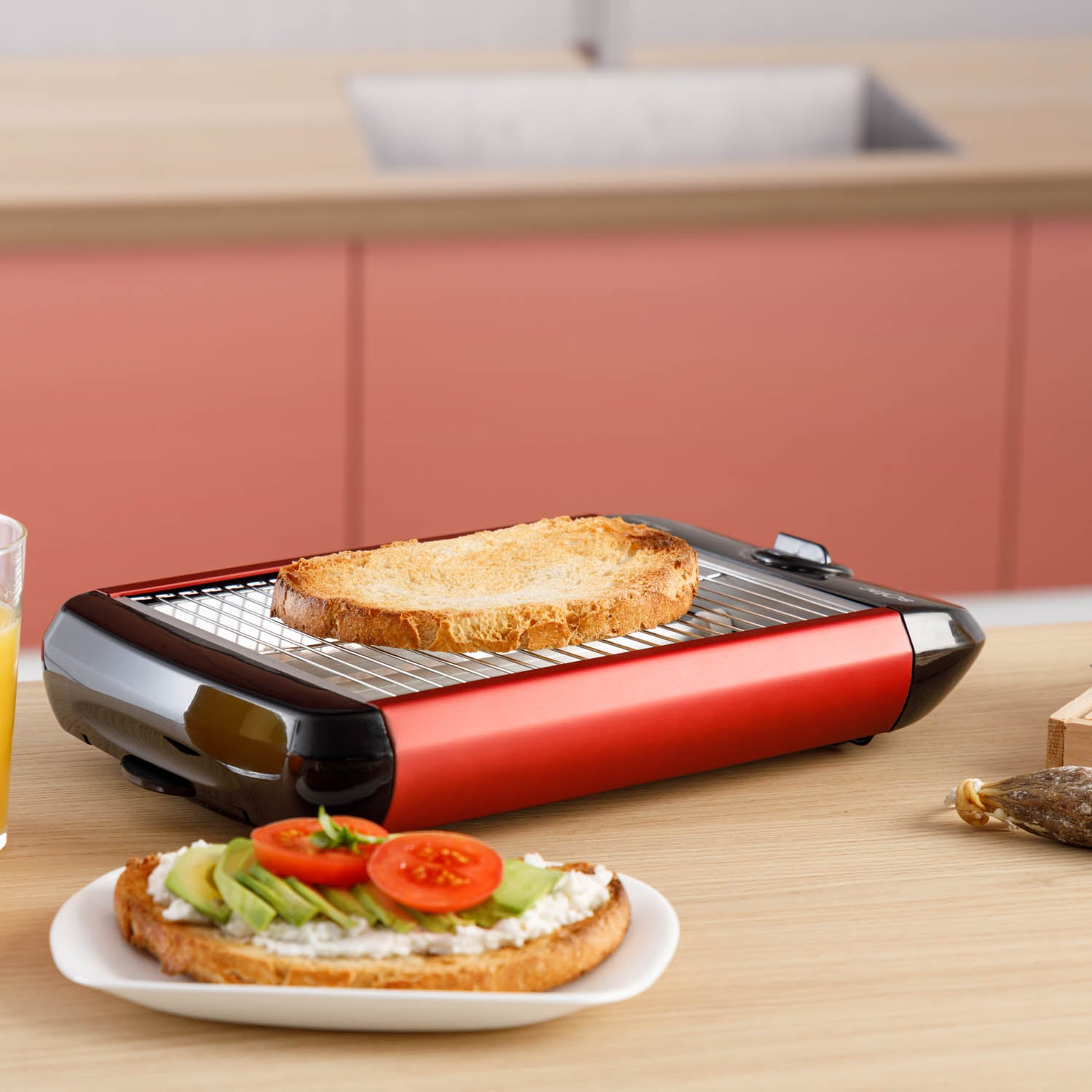 Czerwony i czarny toster. Tost na górze, z talerzem tostów i awokado na stole.