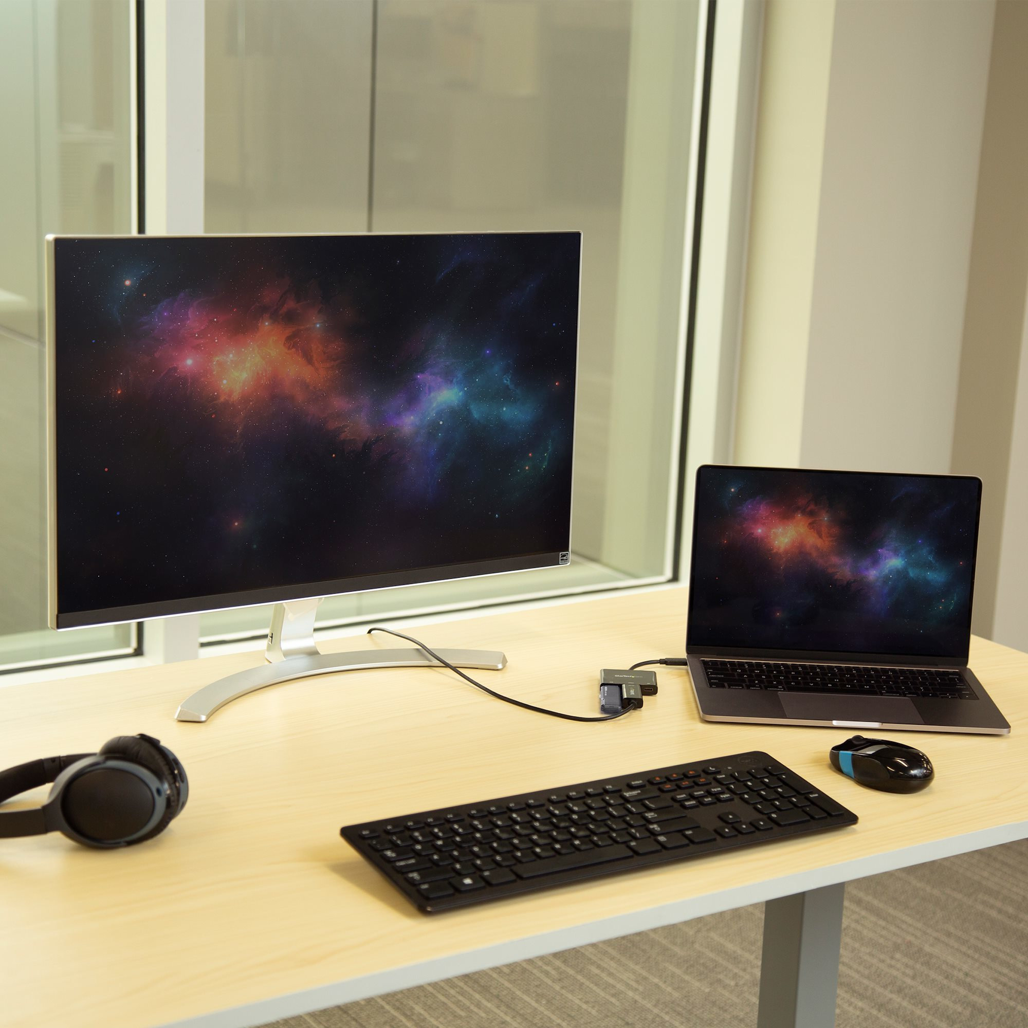 Configurazione scrivania con monitor, laptop, tastiera, mouse e cuffie. Un'immagine della galassia viene visualizzata su entrambi gli schermi.