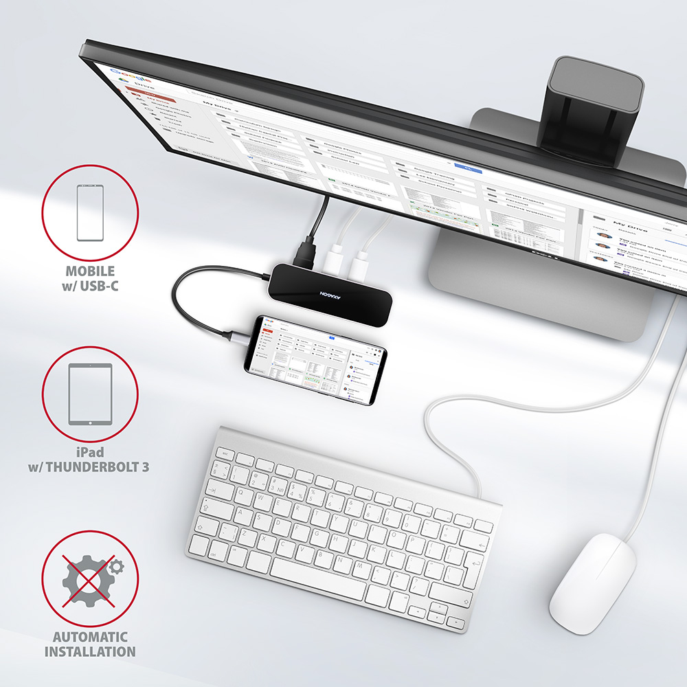 Ein Schreibtisch-Setup mit Monitor, Tastatur, Maus und USB-Hub. Ein Smartphone ist angeschlossen.