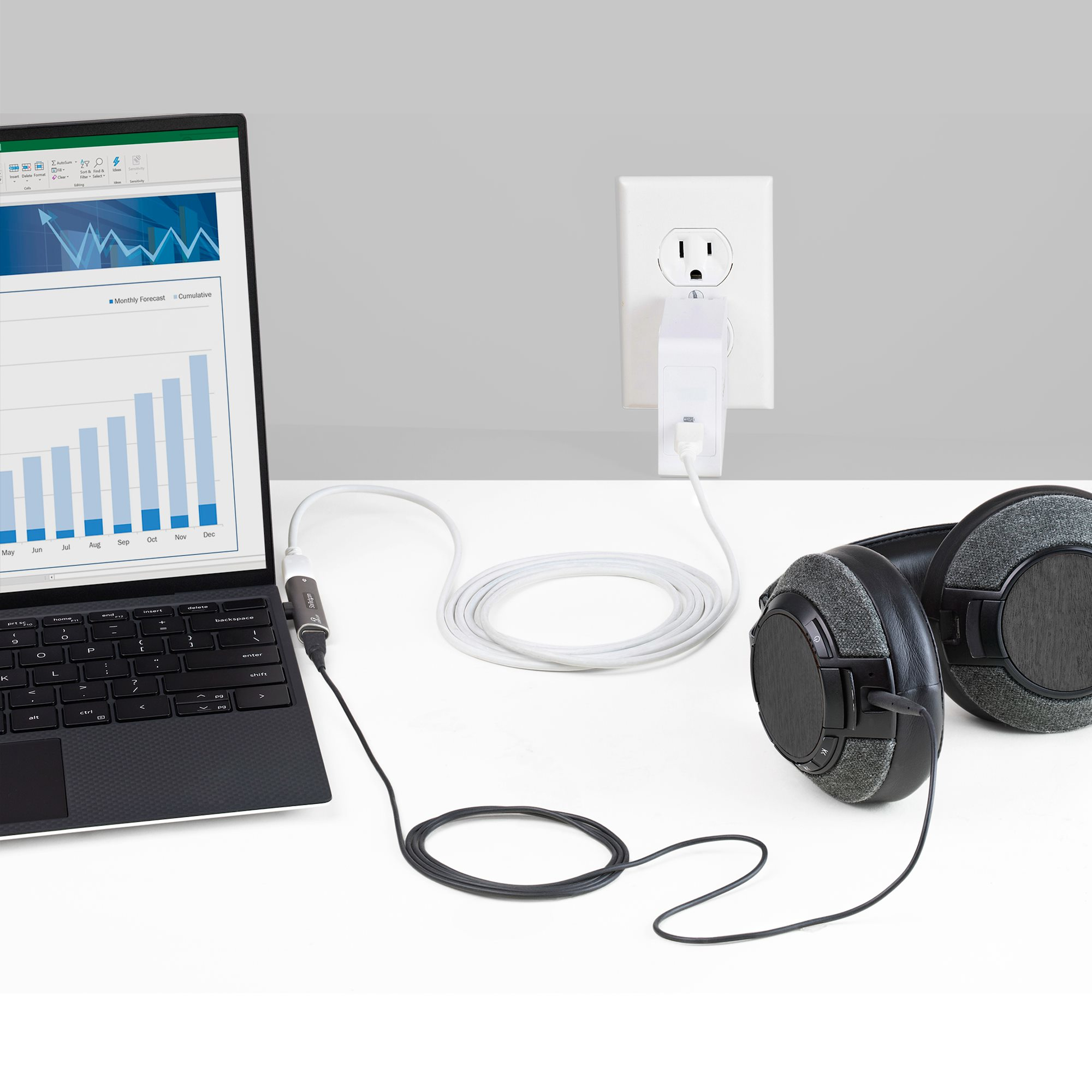 Una computadora portátil, auriculares y un adaptador de corriente enchufado a una toma de corriente. La computadora portátil muestra un gráfico.