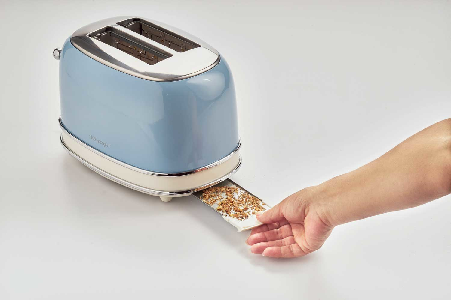 Niebieski toster w stylu vintage. Ręka wyjmuje tackę na okruchy, pokazując okruchy wewnątrz.