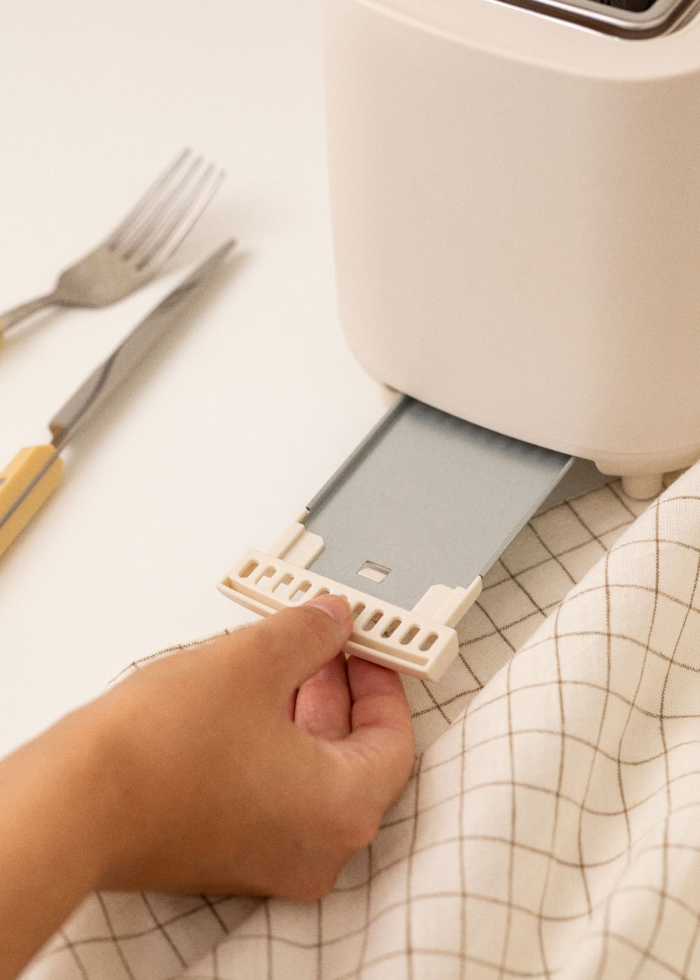 Main tirant un plateau d'un grille-pain. Une fourchette et un couteau sont sur la table.